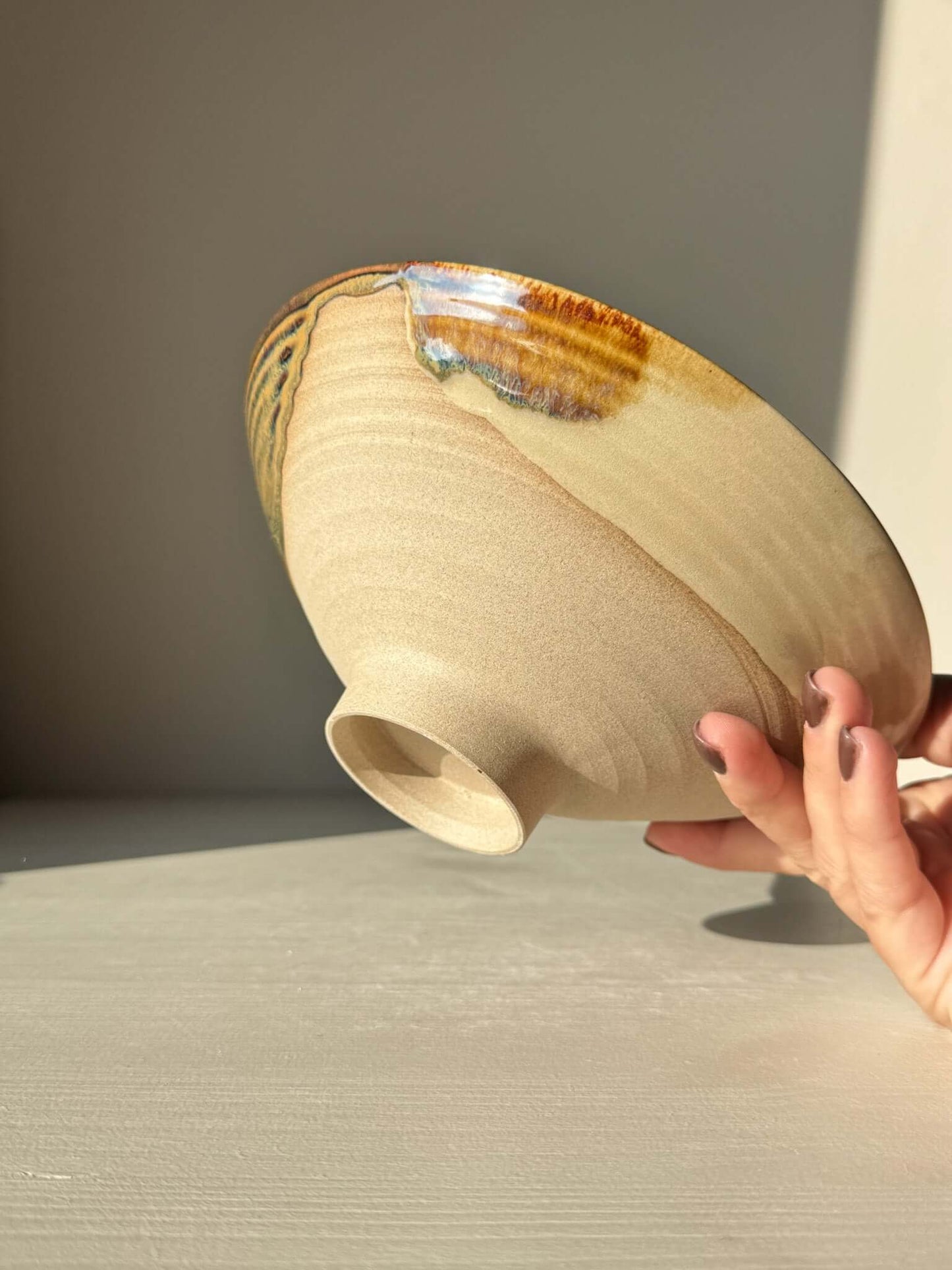 Hand holding a Small Serving Bowl - Inyo Series #01, featuring handmade ceramic with tenmoku, amber, and blue glazes over raw clay base.