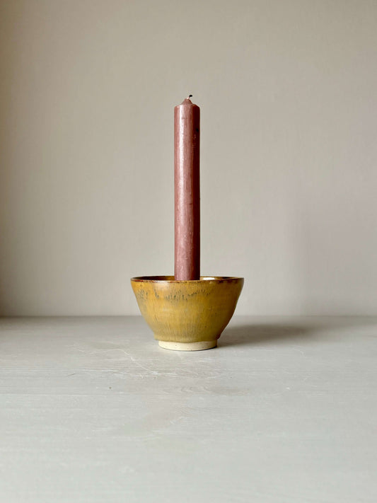 Handmade creamy tenmoku stoneware candlestick holder with a brown candle, 8cm high, 13.5cm diameter, on a neutral background.