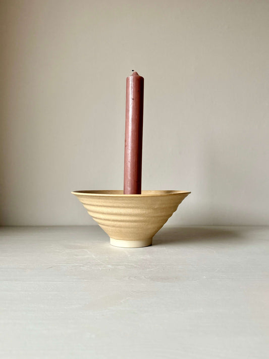 Peach glazed handmade stoneware candlestick holder with brown candle, 9.5cm height and 21cm diameter, on a neutral background.