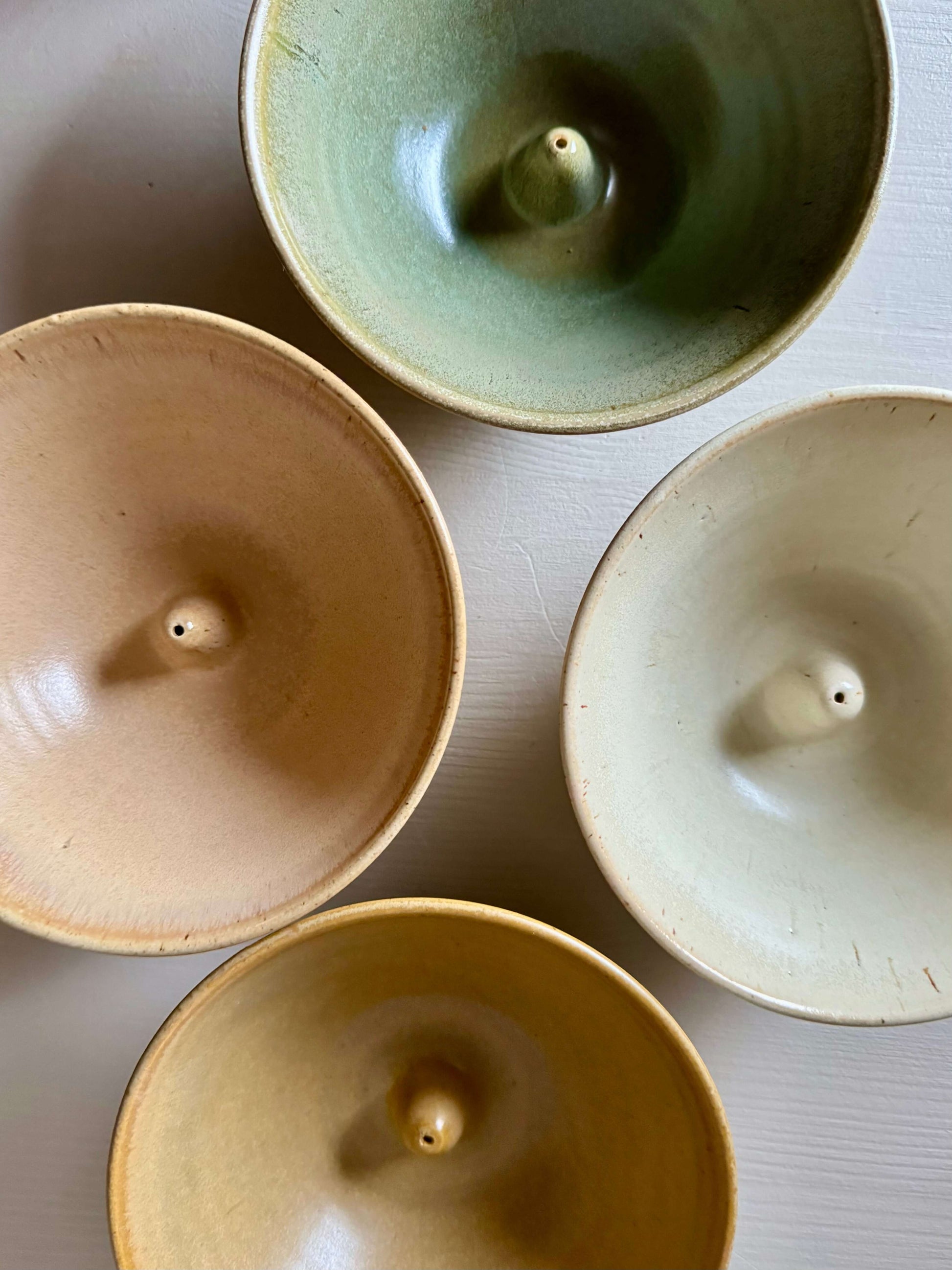 Four colorful handmade stoneware incense holders displayed, showcasing unique peach, green, ivory, and yellow glazes.