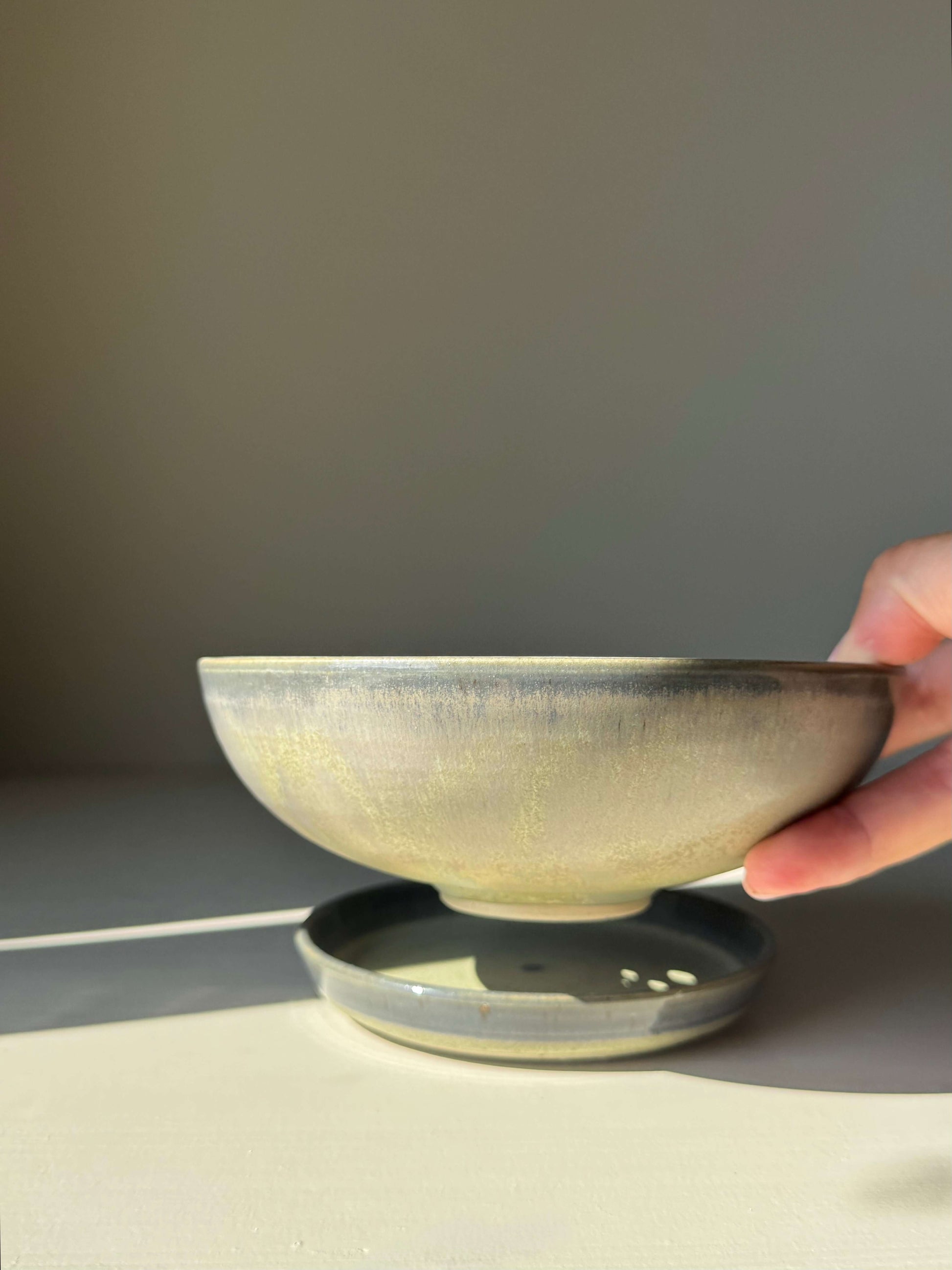 Hand holding a handmade ceramic Berry Bowl - Satin Blue with matching drip plate, showcasing a soft blue-green to smoky grey-blue glaze.