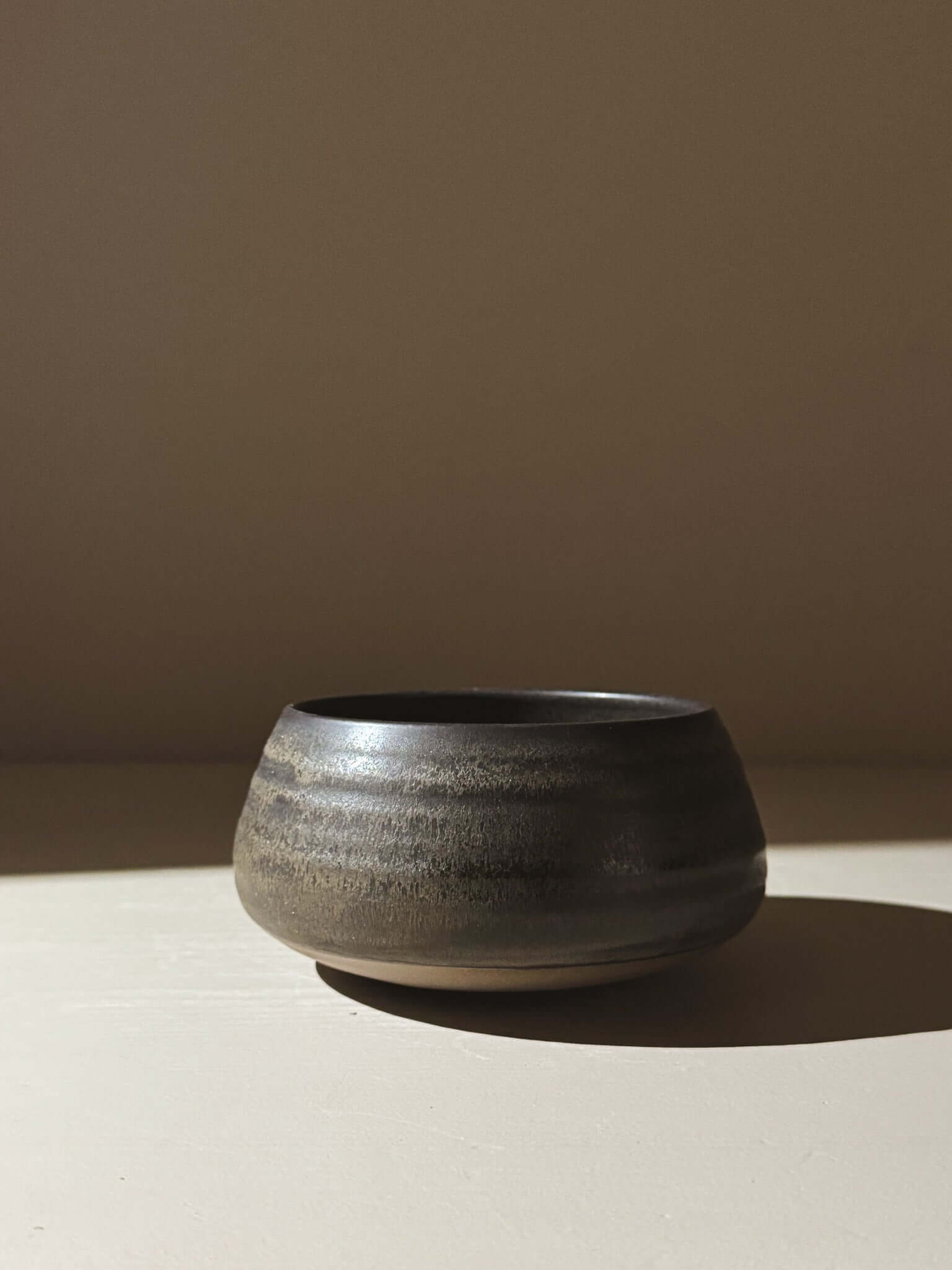 Matcha Bowl - Black Truffle #04 made from stoneware clay with a matte glaze in charcoal and brown tones, placed against a neutral background.