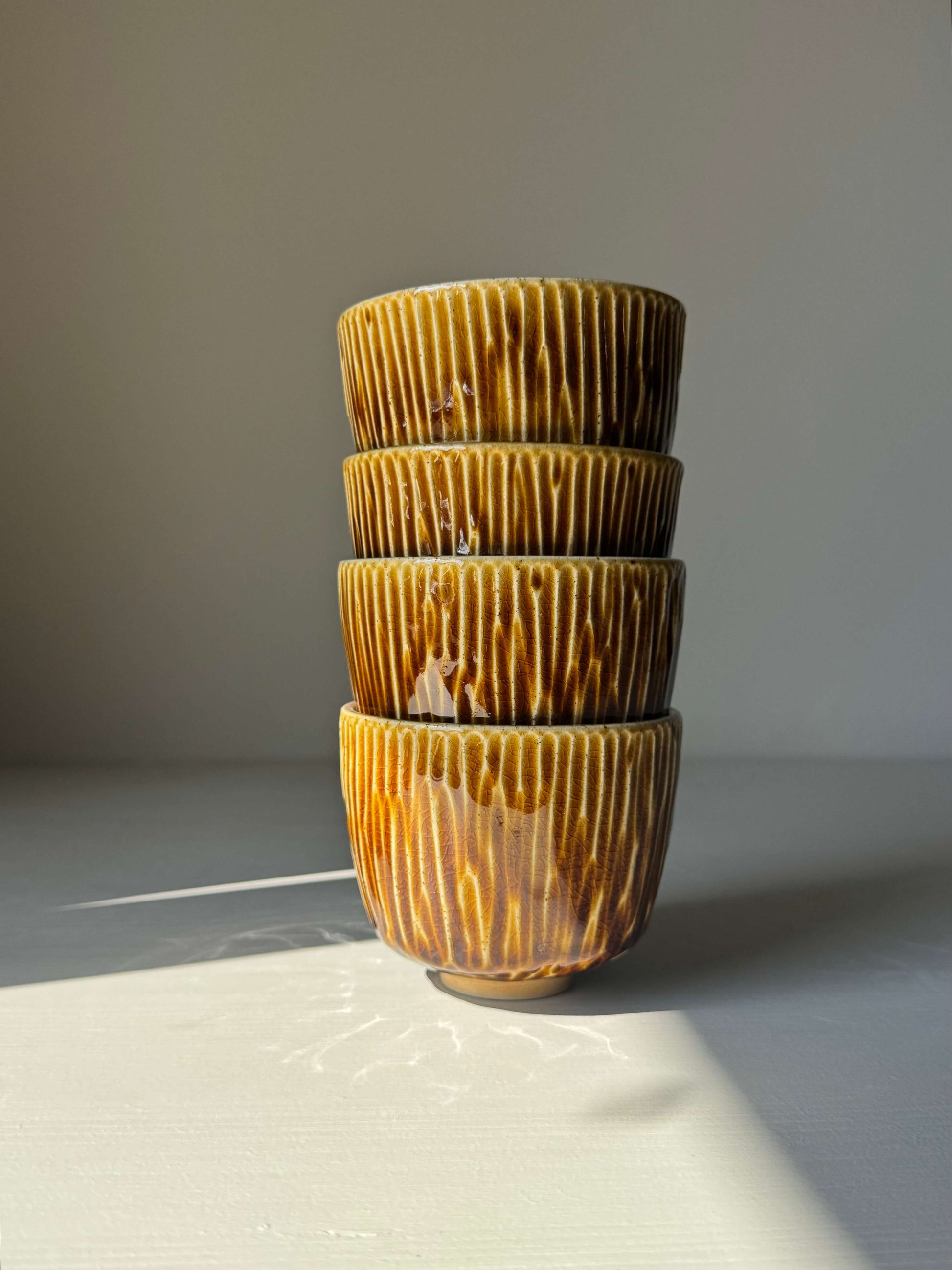 Handmade ceramic Carved Cups - Dark Honey set with a warm golden glaze, stacked together showcasing carved grooves and smooth rim design.