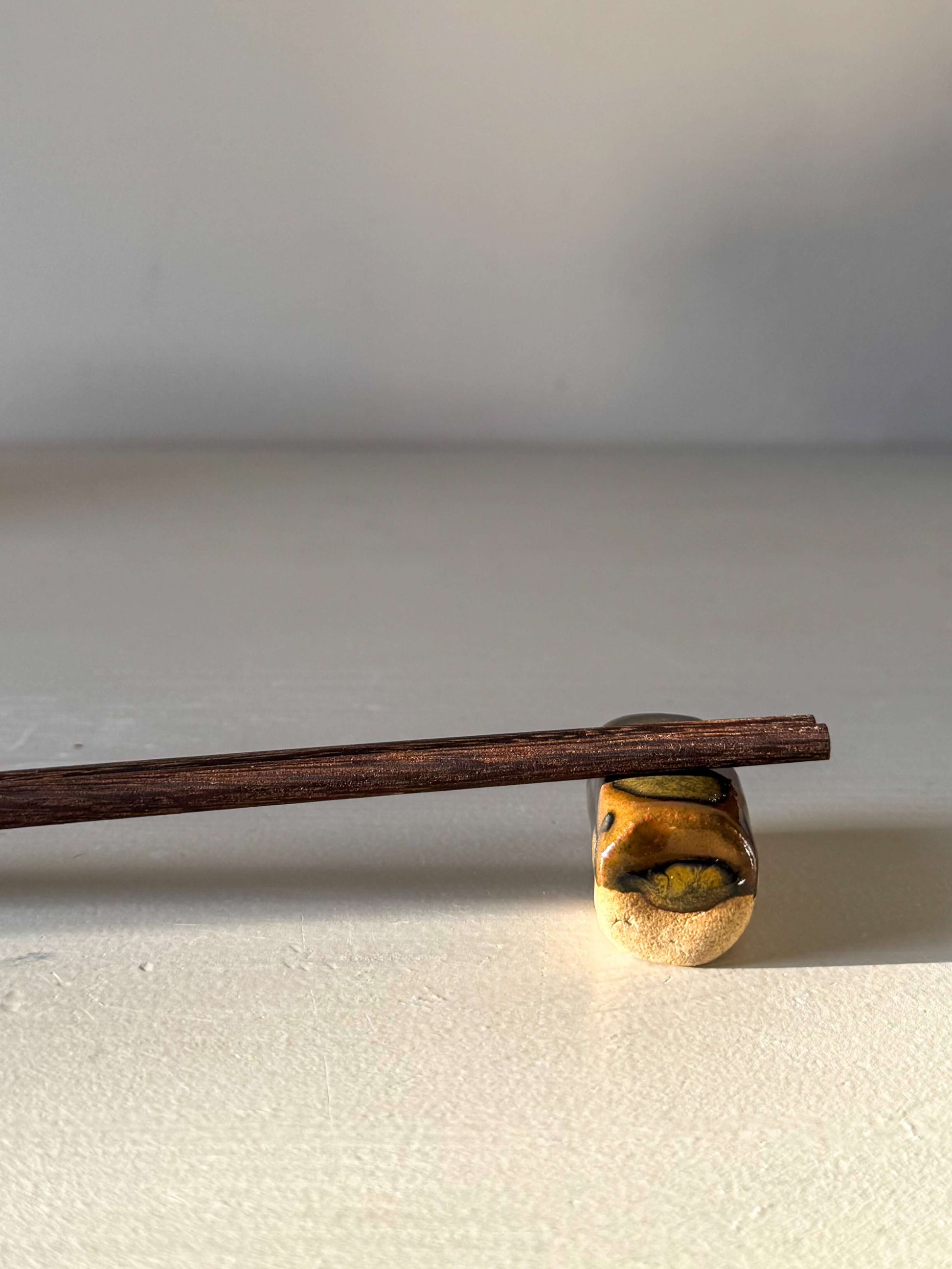 Handmade ceramic Chopstick/Spoon Rest – Inyo with glossy Tenmoku glaze and toffee clay, designed for serene dining experiences.