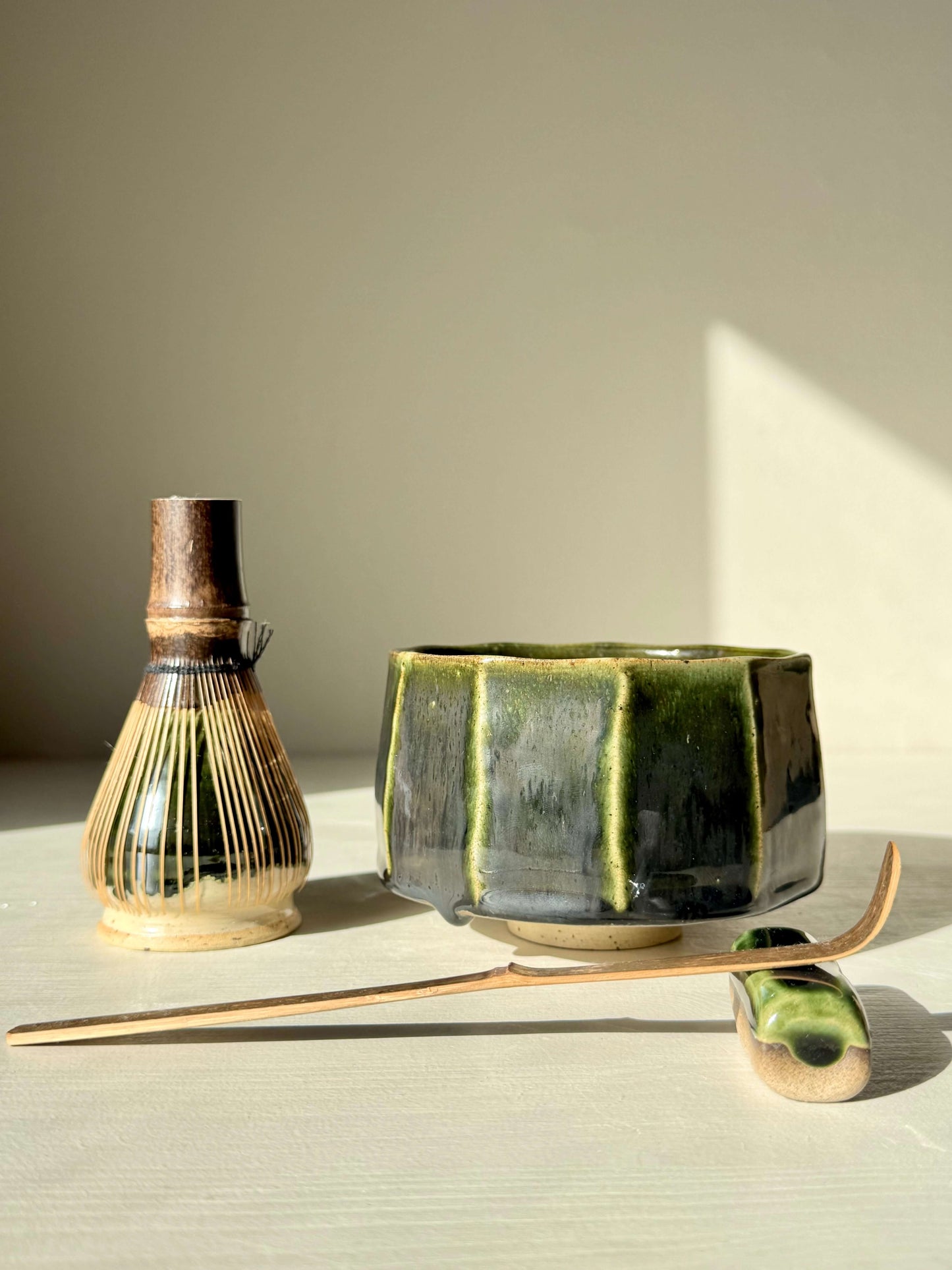 Handmade ceramic Faceted Matcha Bowl - Hinoki Series #01 with deep green glaze, next to a bamboo whisk and spoon.