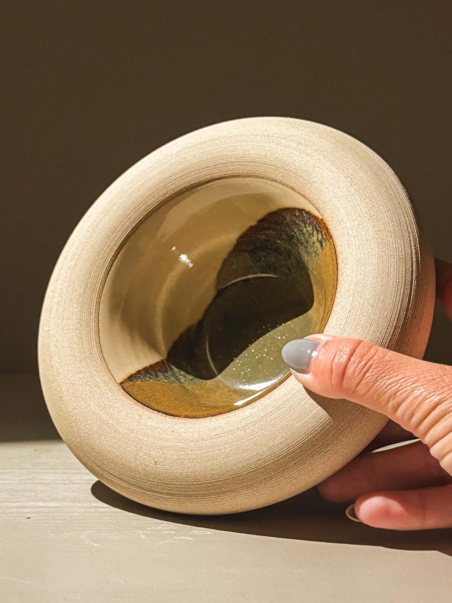 Hand holding a handmade stoneware double-walled bowl, showcasing the unique glazes and raw toffee-toned clay design.
