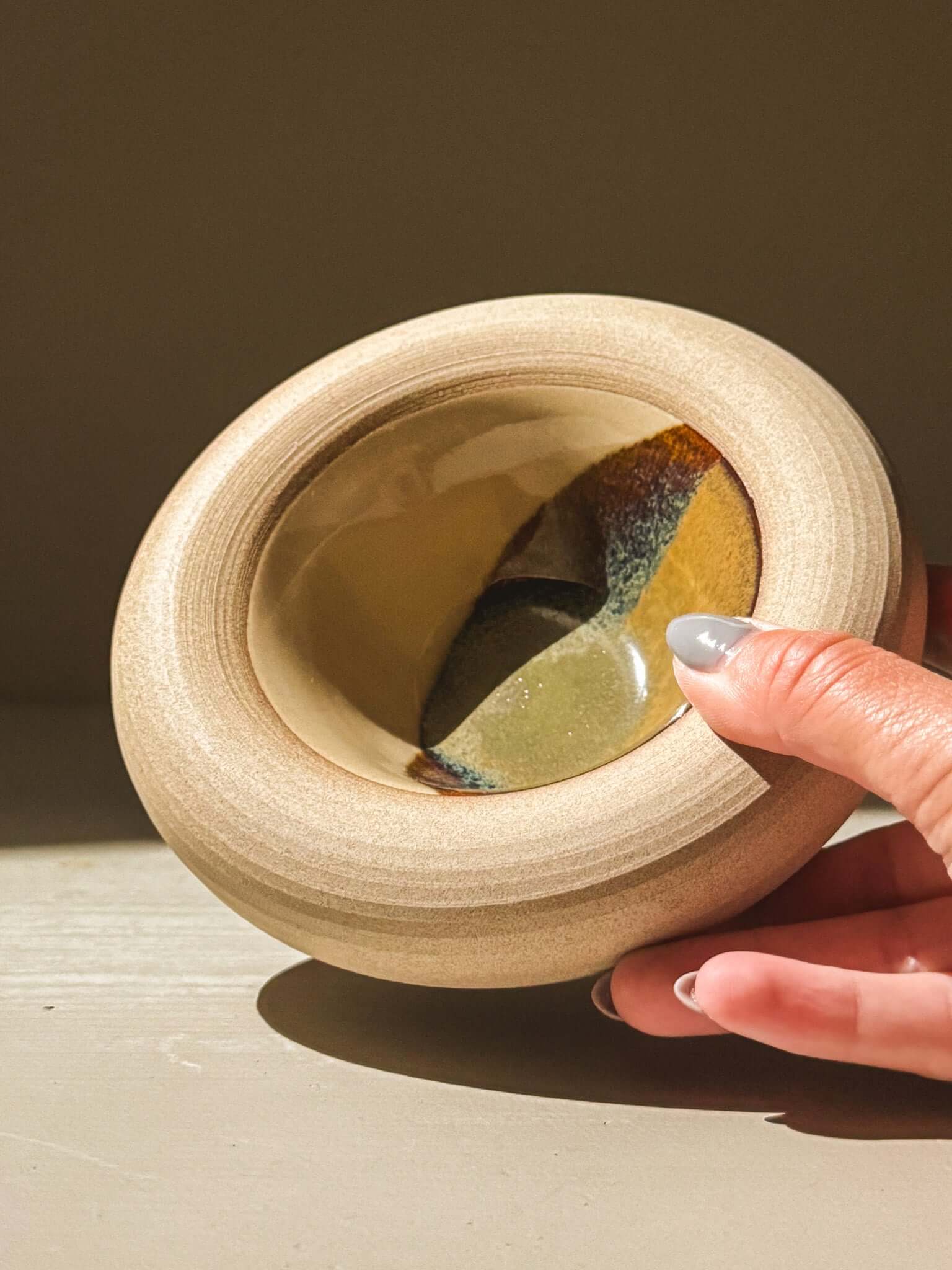 Hand touching handmade stoneware bowl with double walls, toffee-toned clay exterior, and glazed interior from Inyo Series.