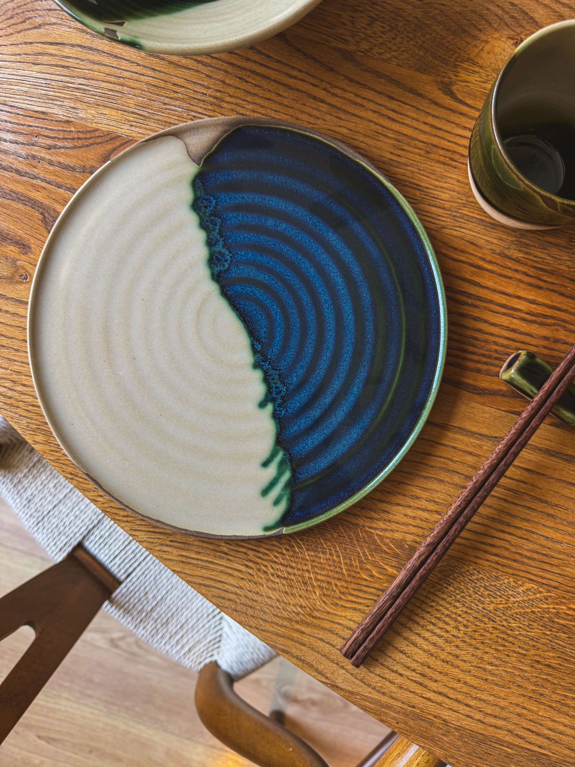Flat Round Plate – Mori, handmade ceramic with green toffee glaze, on a wooden table with chopsticks, highlighting unique design.