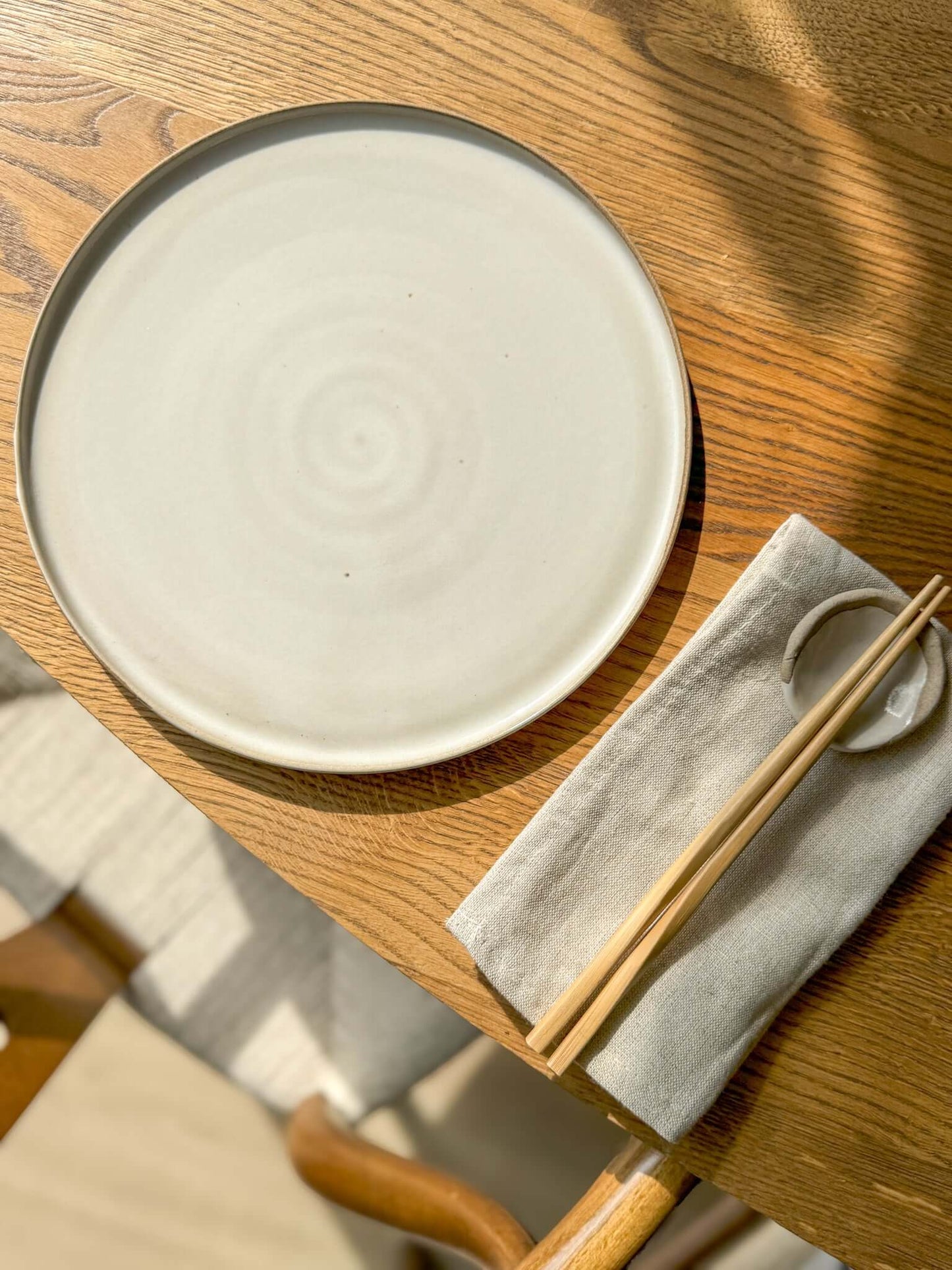 Flat Round Plate – Yuki Series ceramic plate on a wooden table with chopsticks, showcasing handmade craftsmanship and elegance.