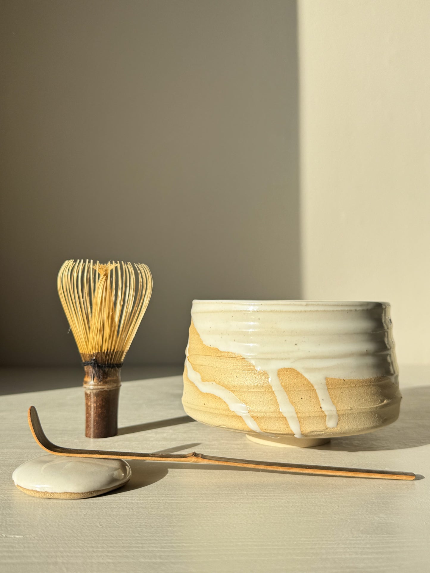 Matcha Bowl – Glossy White #03 with speckled stoneware clay and glossy glaze, showcasing whisk and tea accessories in natural light.