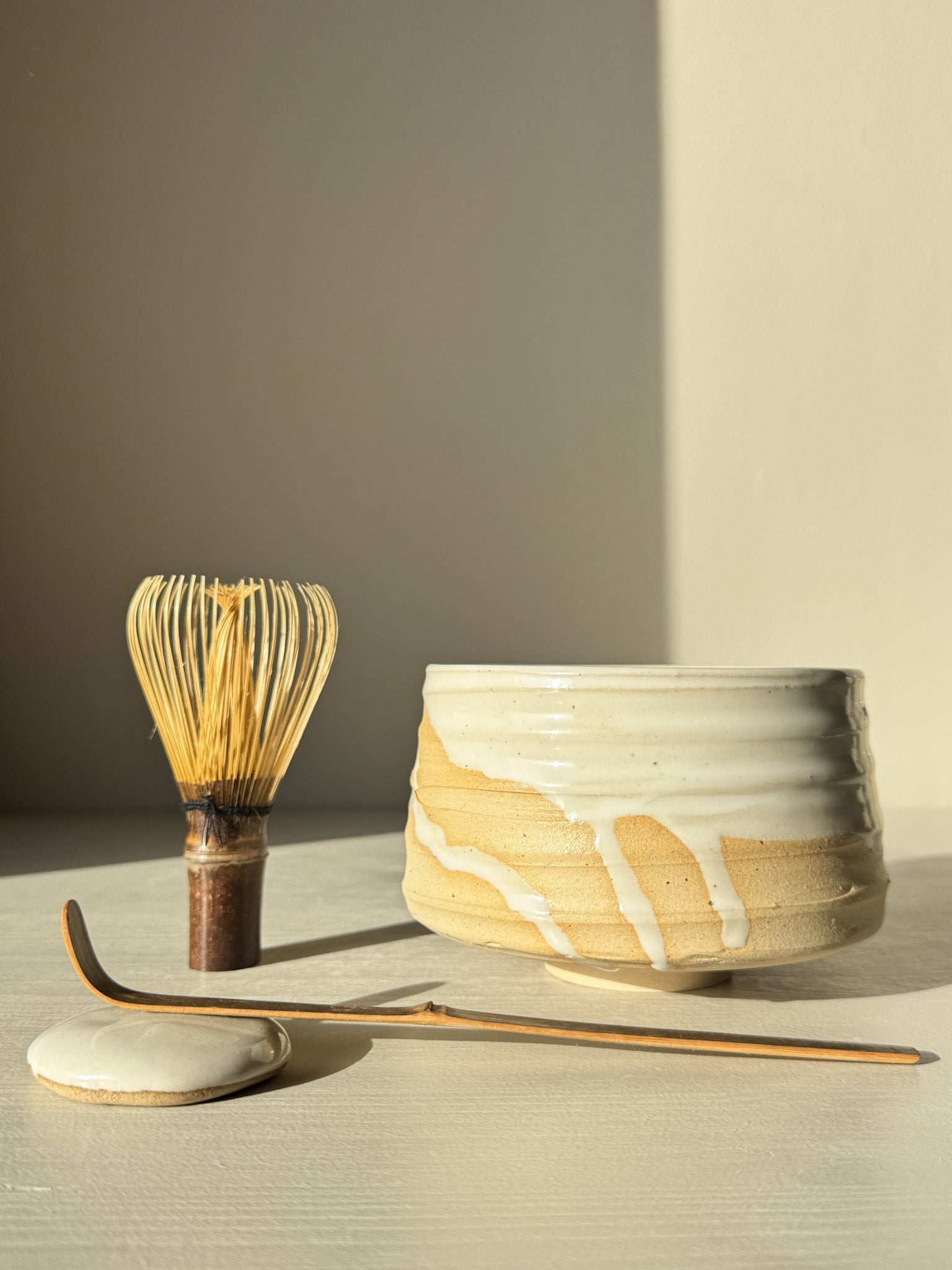 Matcha Bowl – Glossy White #03 with speckled stoneware clay and glossy glaze, showcasing whisk and tea accessories in natural light.