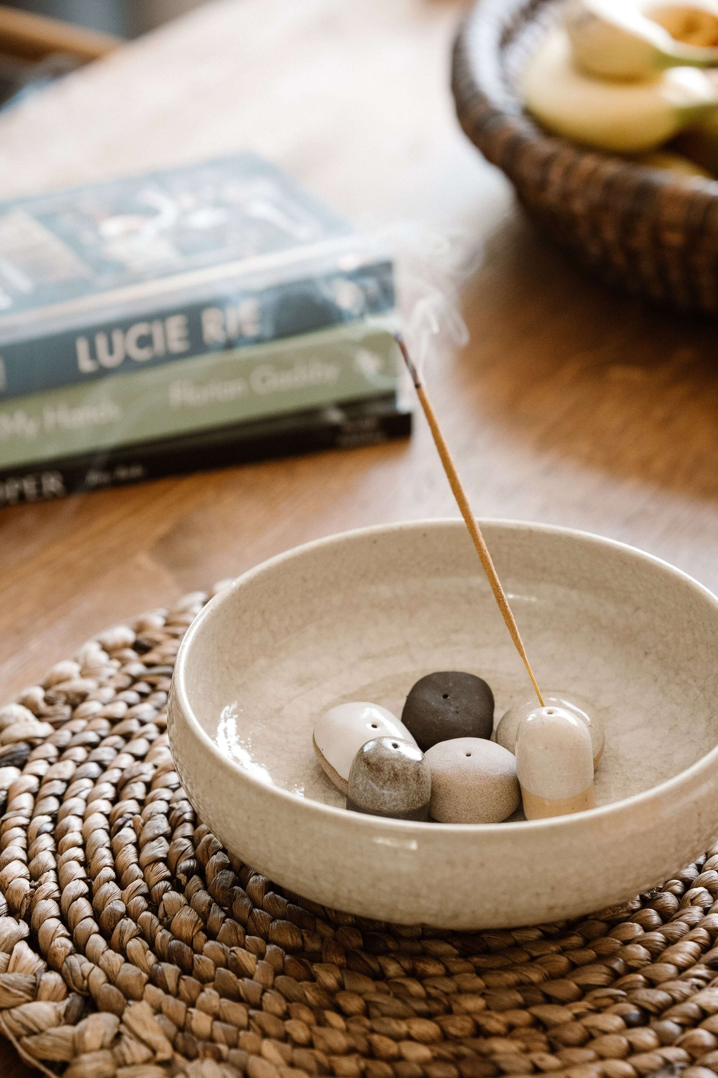 Incense Holder Pebbles in a bowl, handmade ceramic with natural glaze, holding a burning incense stick on a woven mat.