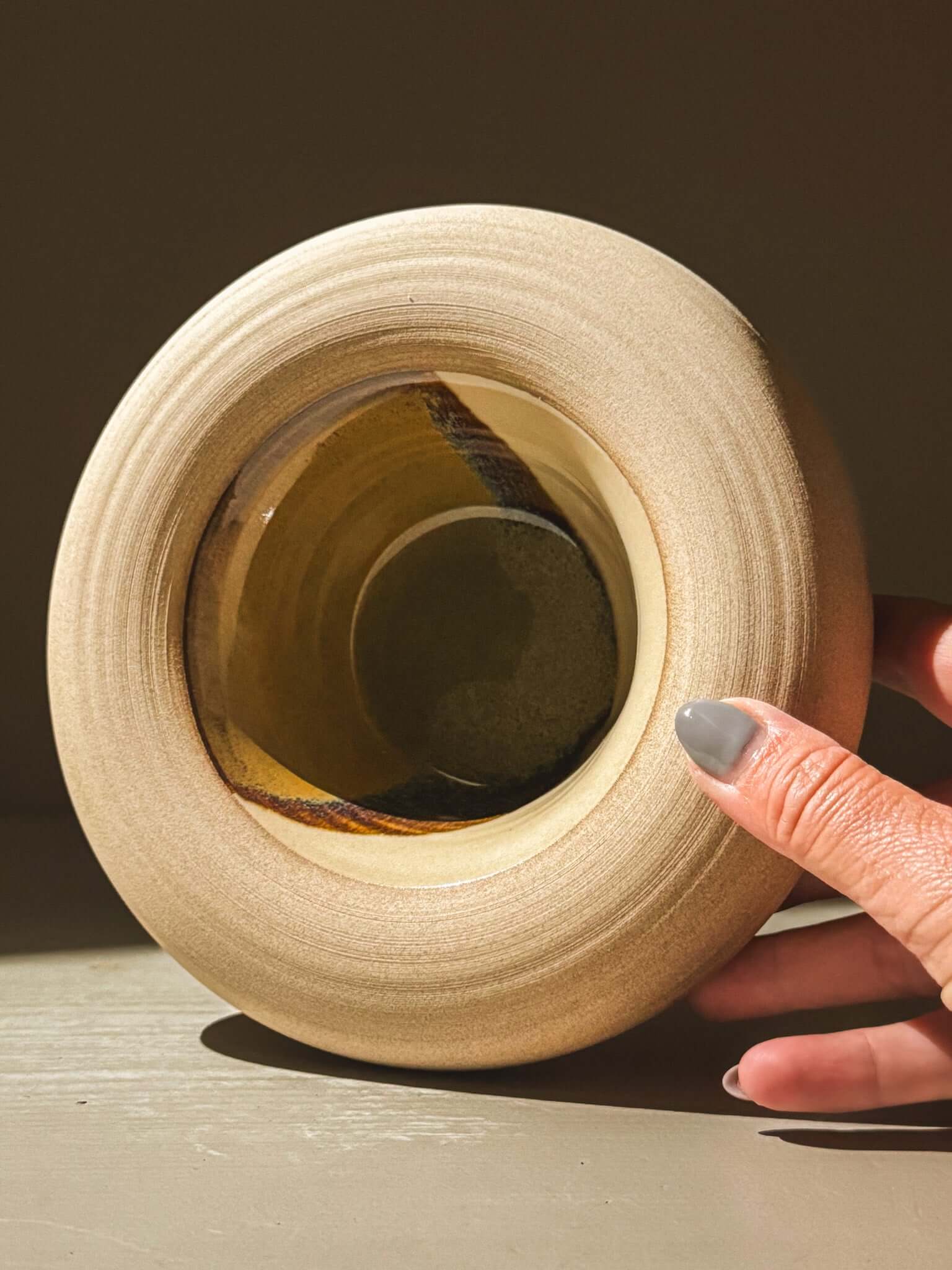 Handcrafted double-walled ceramic bowl from Inyo Series with toffee-toned clay and tenmoku-glazed interior being held gently.