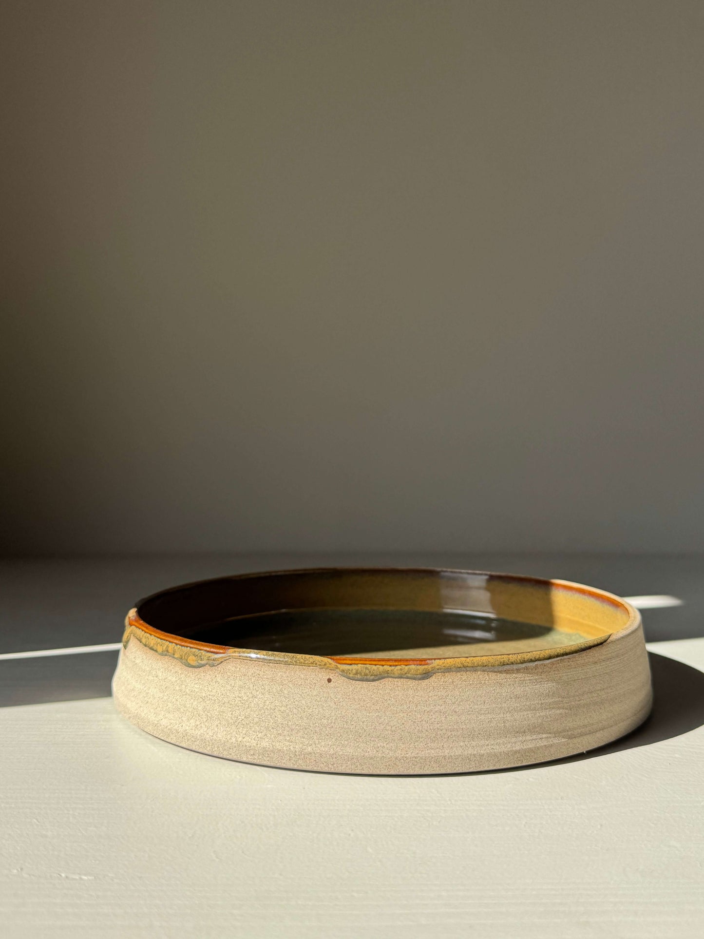 Plate – Inyo Series, handmade ceramic plate with glossy tenmoku glaze and raw clay edge in natural lighting, showcasing a versatile design.