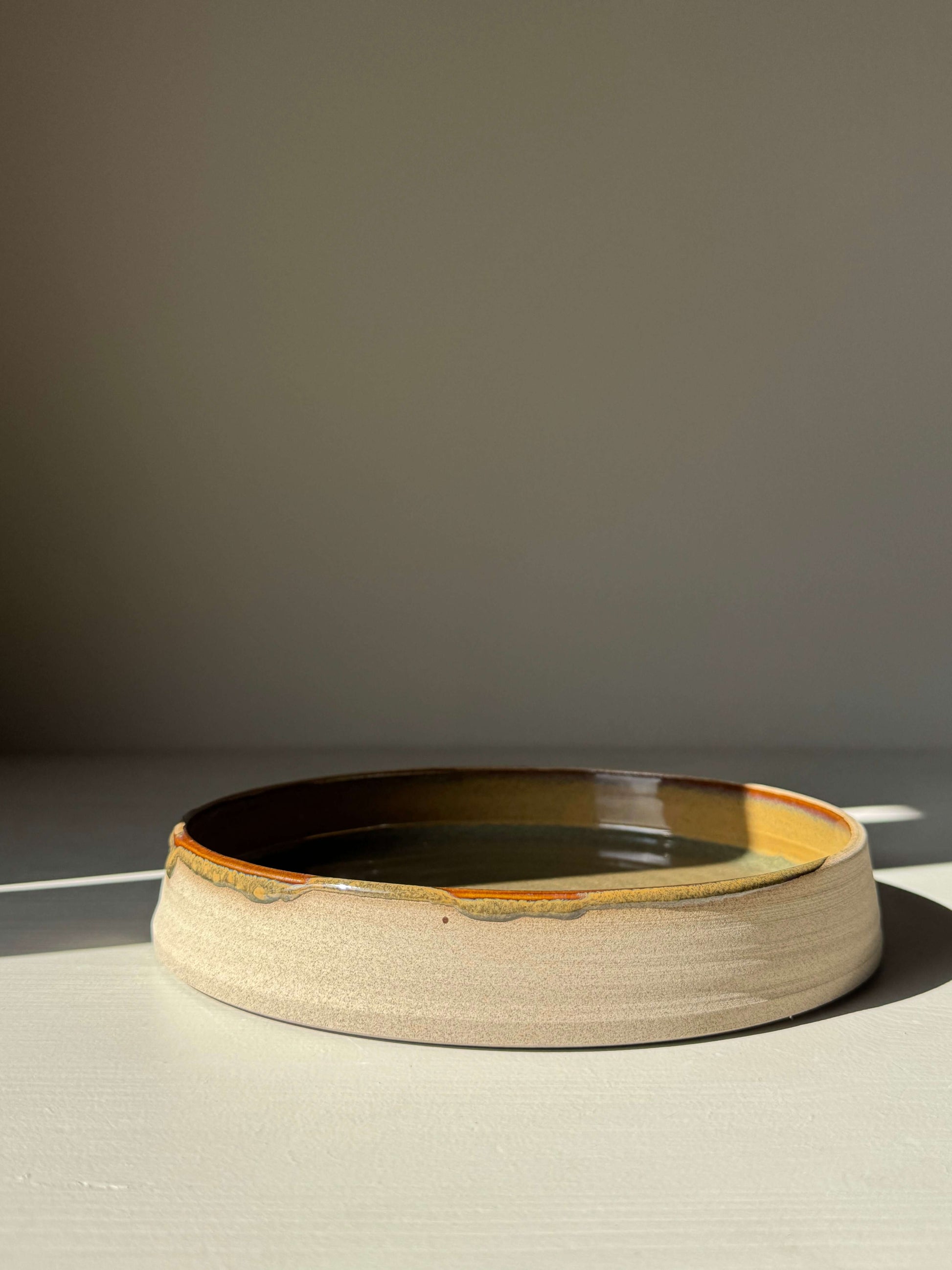 Plate – Inyo Series, handmade ceramic plate with glossy tenmoku glaze and raw clay edge in natural lighting, showcasing a versatile design.