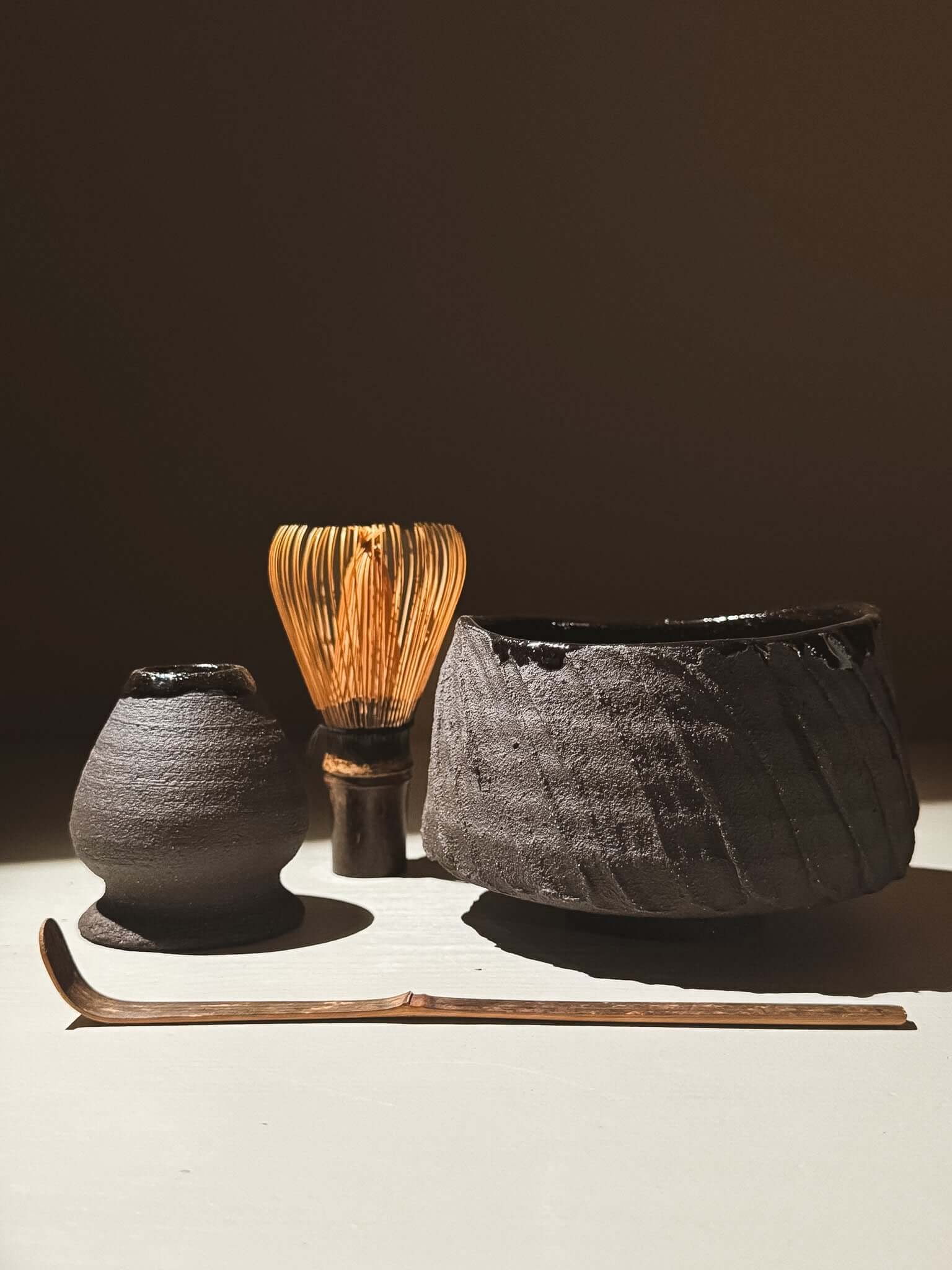 Kuro Matcha Bowl #05 with volcanic stone texture, dark glaze, and tea whisk on a light surface