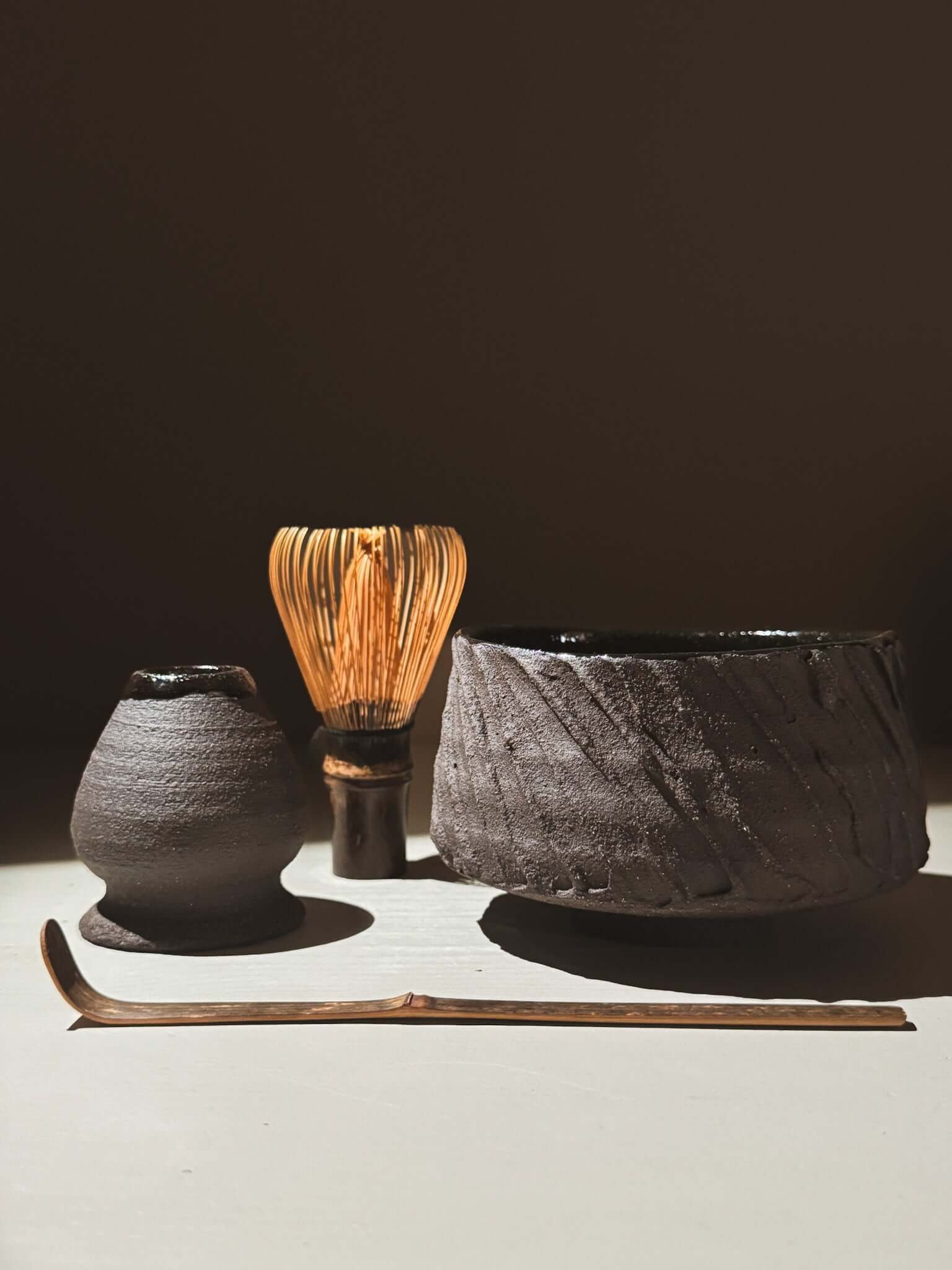 Kuro Matcha Bowl #01 with chasen whisk and scoop, showcasing textured dark brown slip and glossy dark glaze finish.
