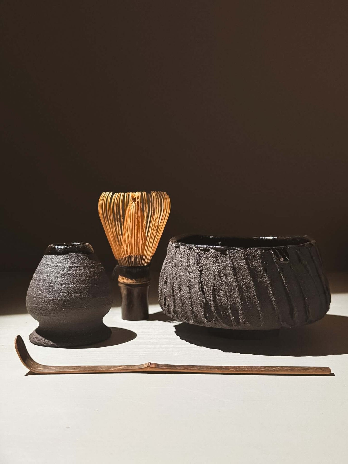 Kuro Matcha Bowl #02 with whisk and tools on display, showcasing volcanic stone-inspired texture and dark glossy finish.