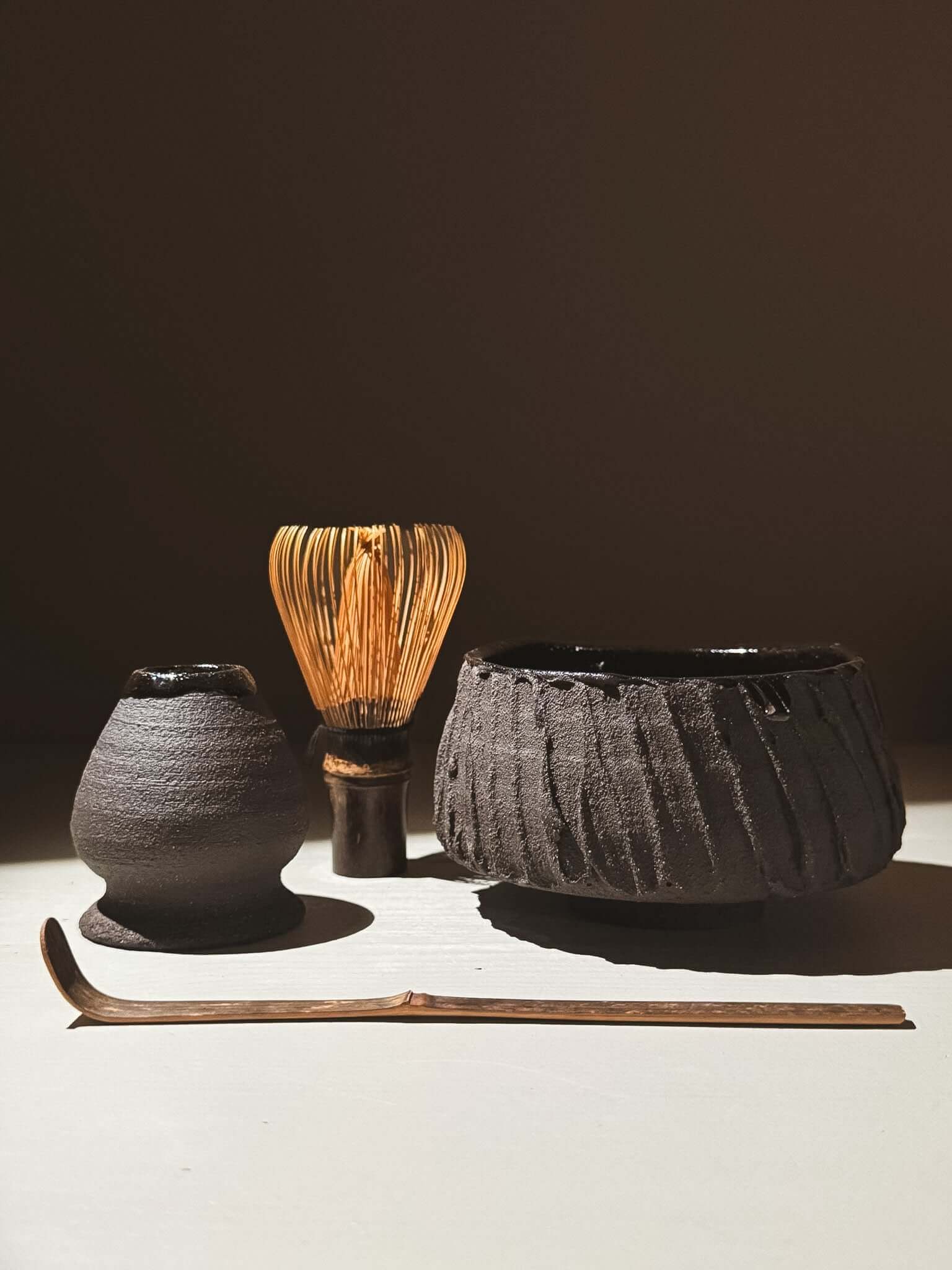 Kuro Matcha Bowl #02 with whisk and tools on display, showcasing volcanic stone-inspired texture and dark glossy finish.