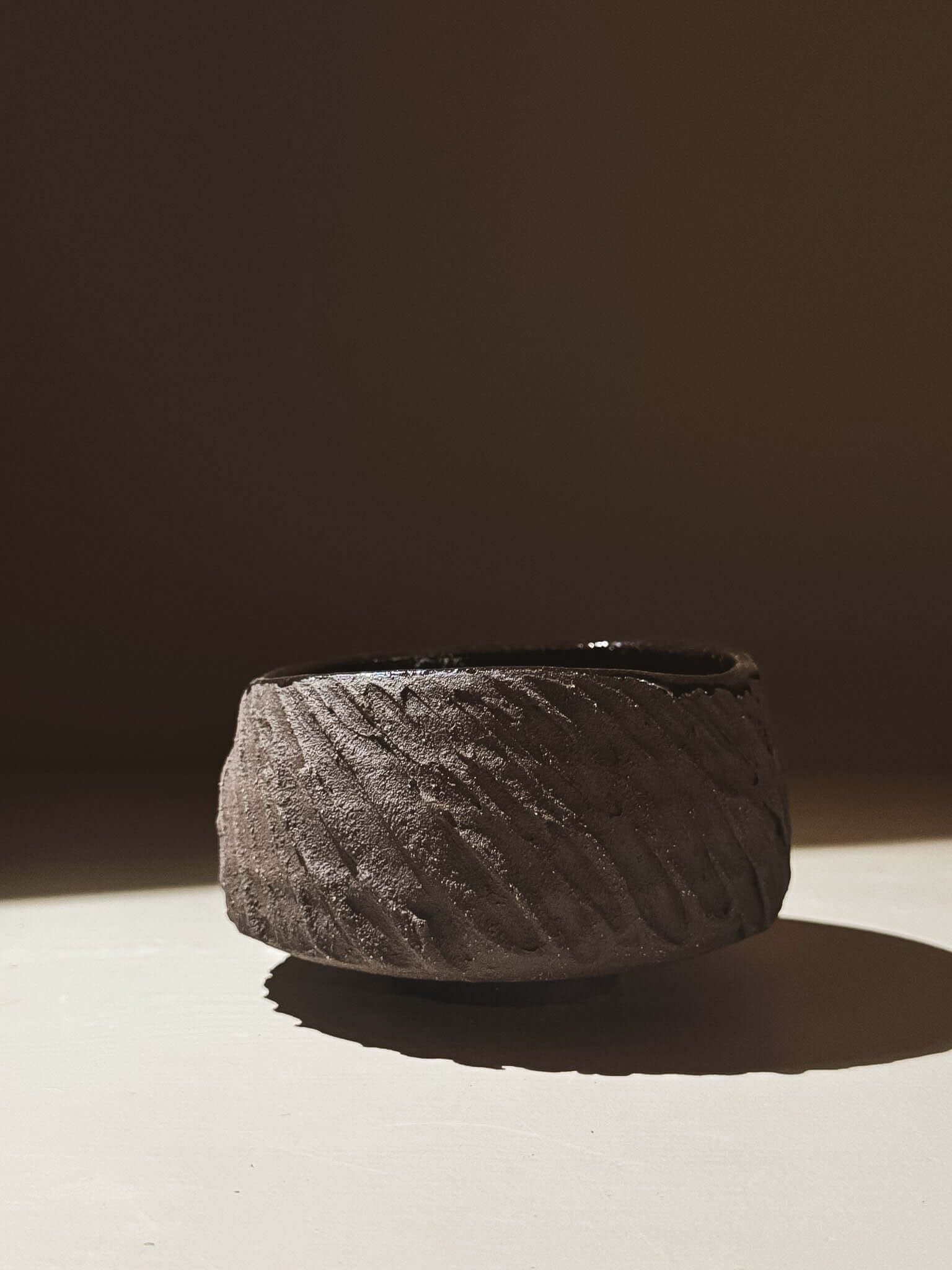 Kuro Matcha Bowl #08 with textured dark brown slip and glossy dark glaze contrasted by light, inspired by volcanic stone.