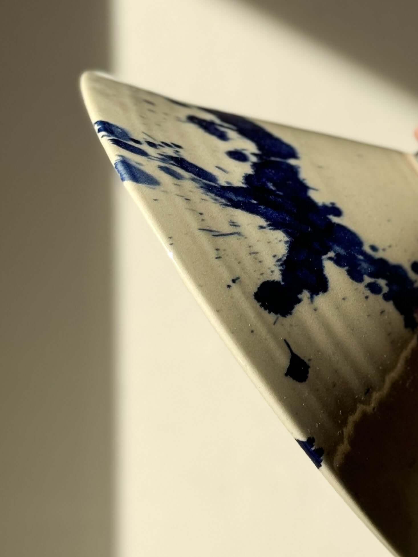 Close-up of a handmade ceramic lamp shade with a beige glaze and bold cobalt blue brushstroke design, showcasing its smooth, curved edge and artistic finish.