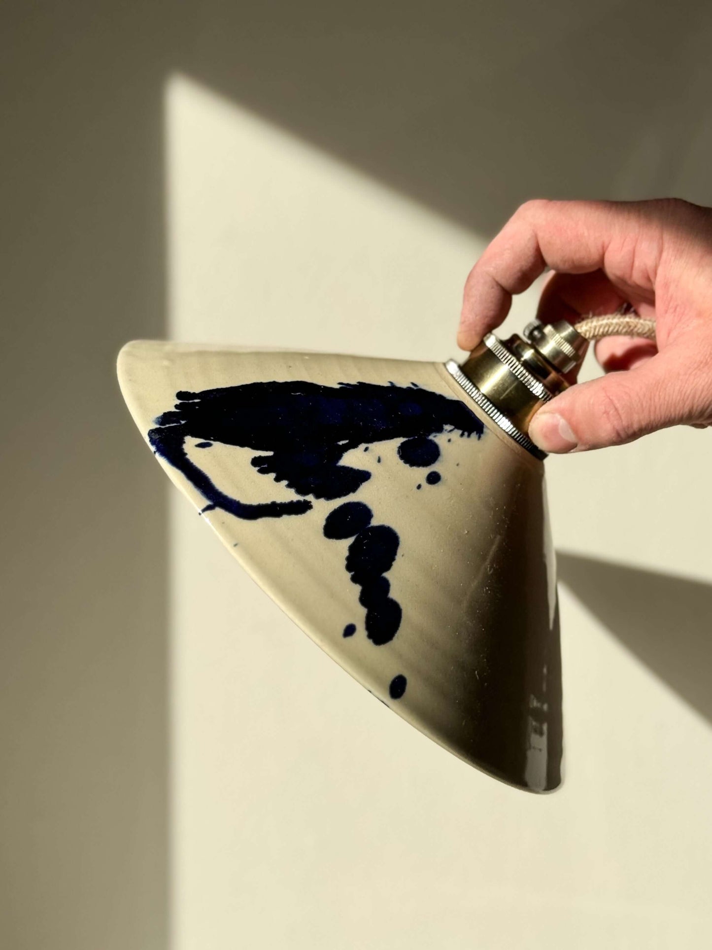 Hand holding handmade ceramic lamp shade with cobalt blue splashes, part of Gosu Series, showcasing unique artistic design.