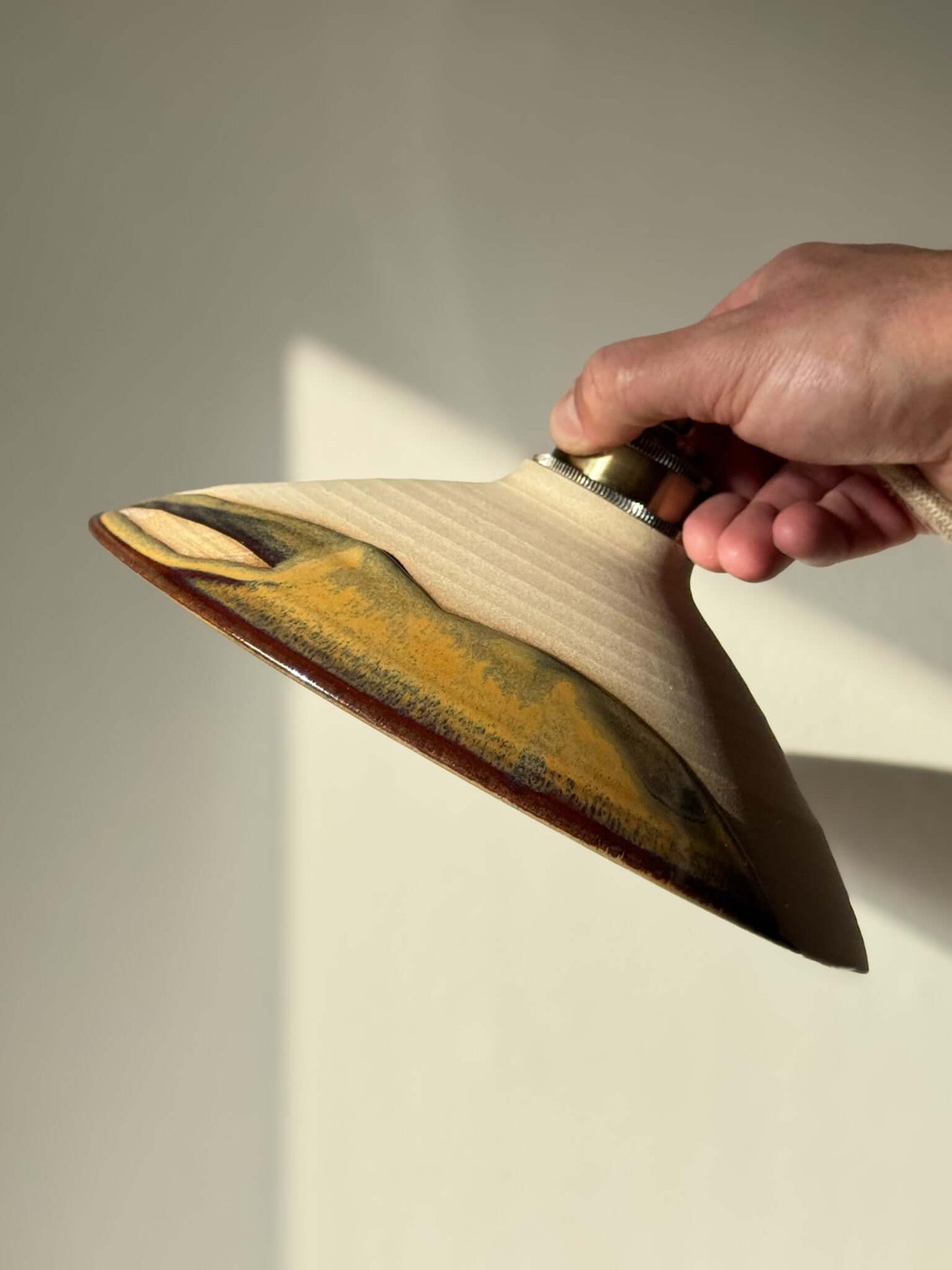 Hand holding Ceramic Lamp Shade – Inyo #02, handmade ceramic with bronze, amber, and blue hues, highlighting raw clay and glossy glaze.
