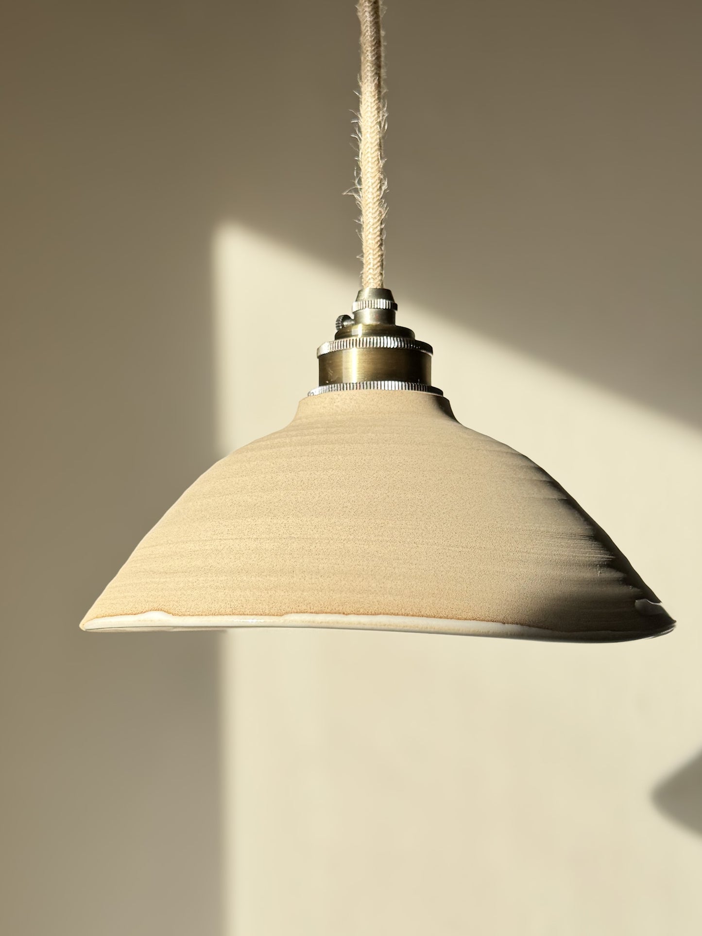 Ceramic Lamp Shade – Yuki #02 with glossy white glaze and raw clay, showing its slightly slanted and organic shape against a soft light.