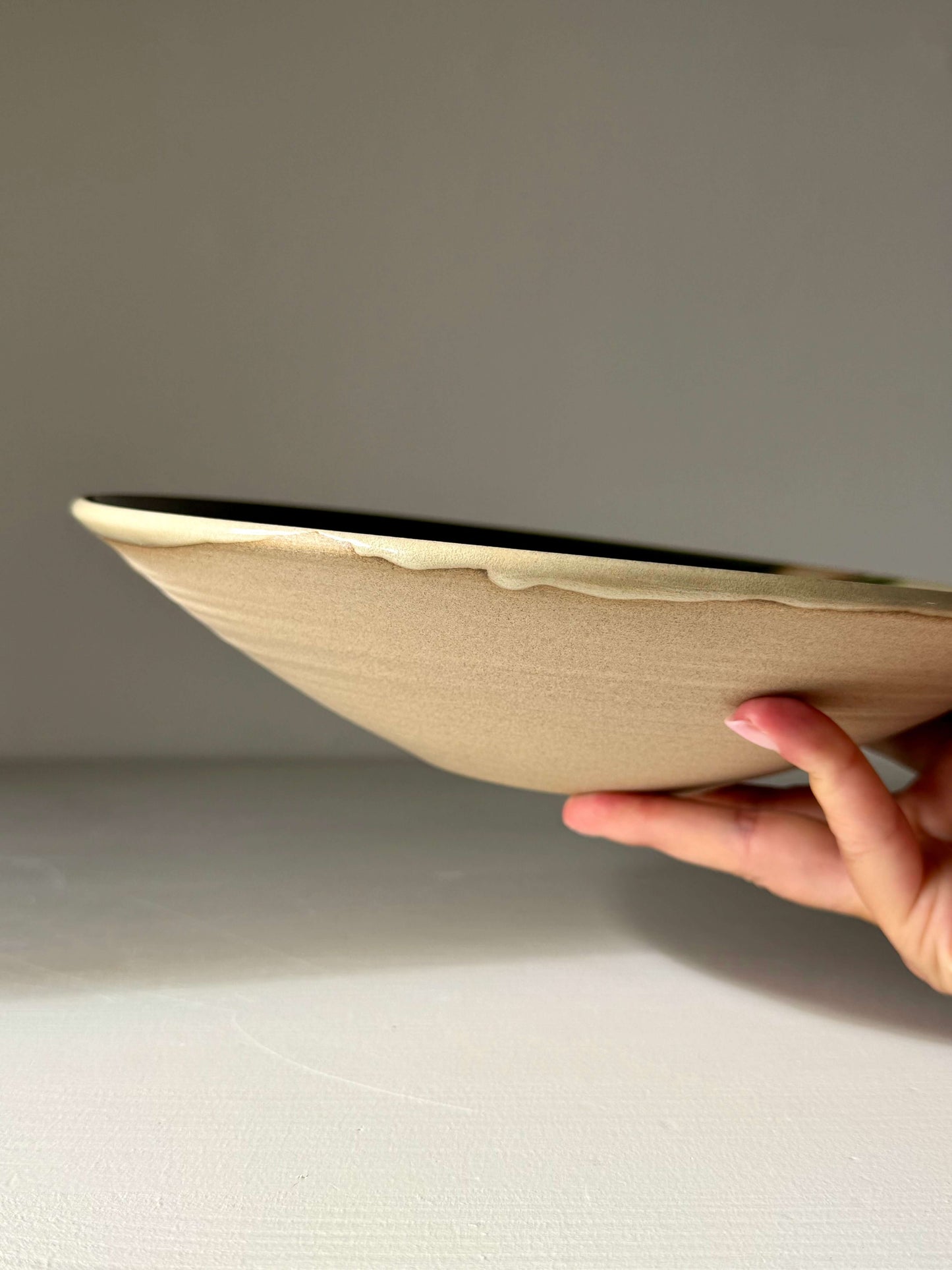 Hand holding a handmade ceramic Large Shallow Bowl - Mori Series with a flowing green glaze design.