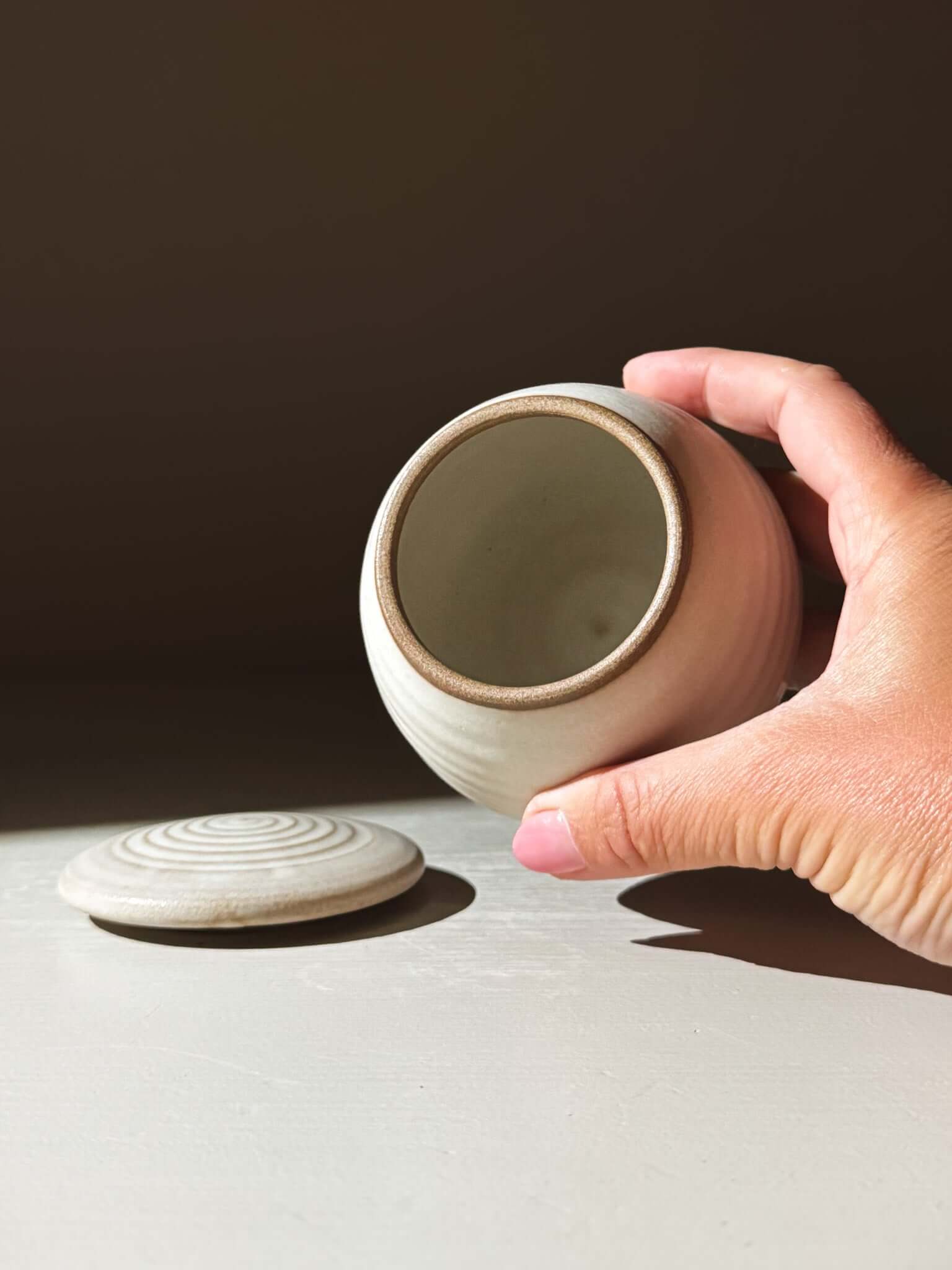 Hand holding ceramic Lidded Jar - Eggshell #03, showcasing handmade pottery with lid beside, perfect for storing treasures.
