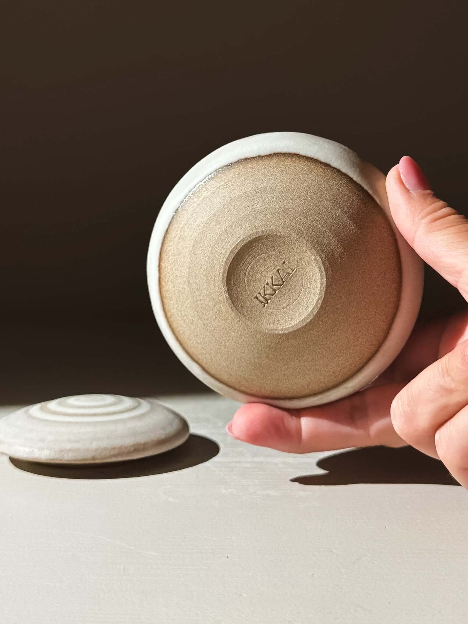 Holding the handmade ceramic lid of Lidded Jar - Eggshell #04, showcasing intricate pottery design. Perfect for storing treasures.