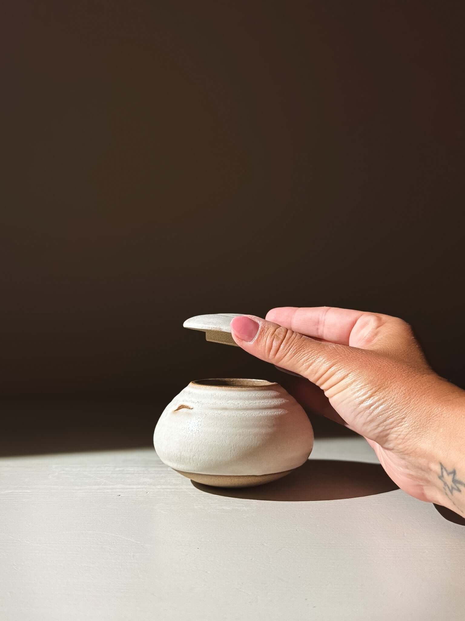 Person opening Lidded Jar - Eggshell #04, a handmade ceramic piece in pottery, displayed in warm light.