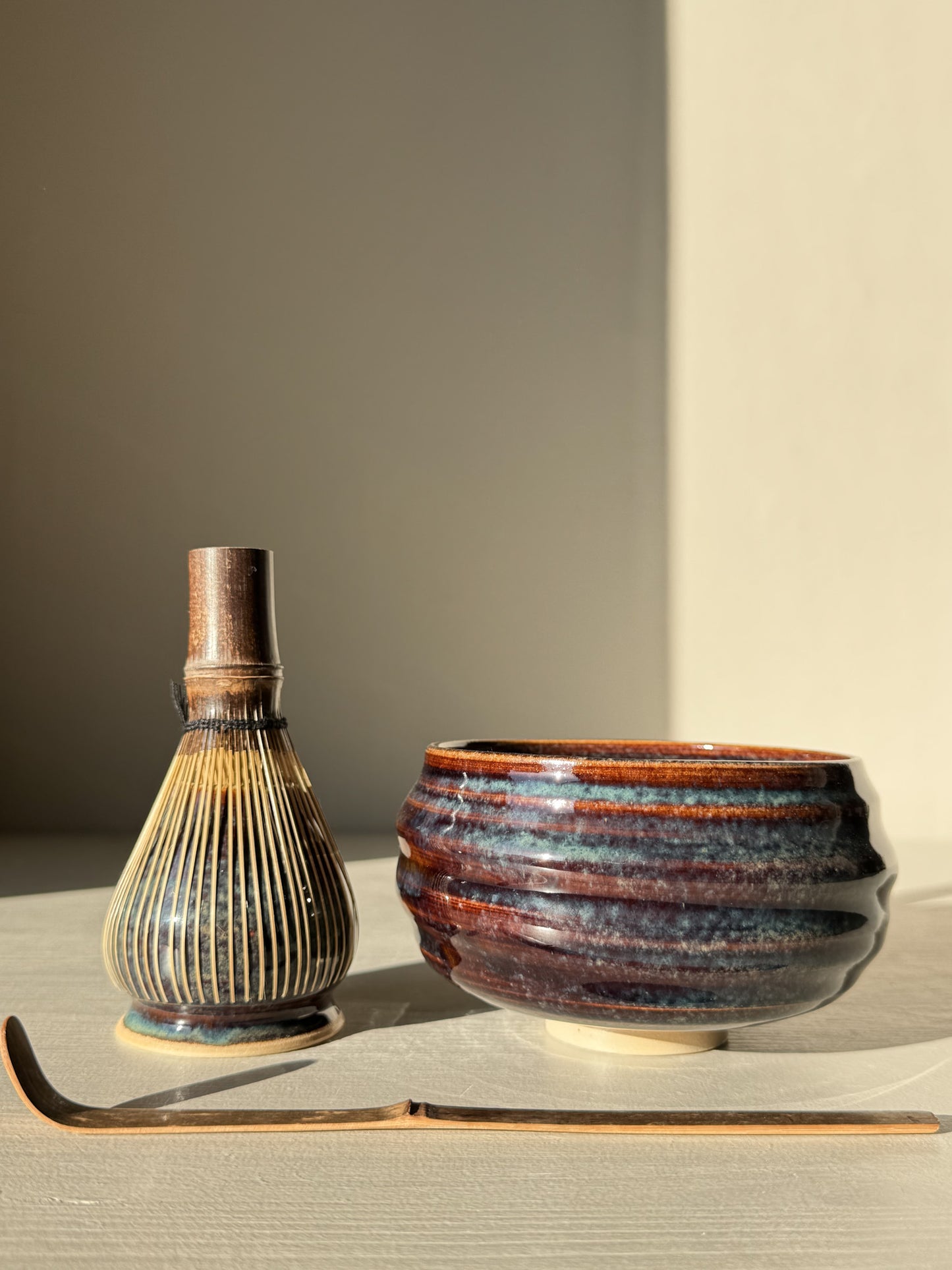 Matcha Bowl - Glossy Blue #02 with chasen and chashaku in soft lighting, highlighting the bowl's unique flowing blue design and raised foot.