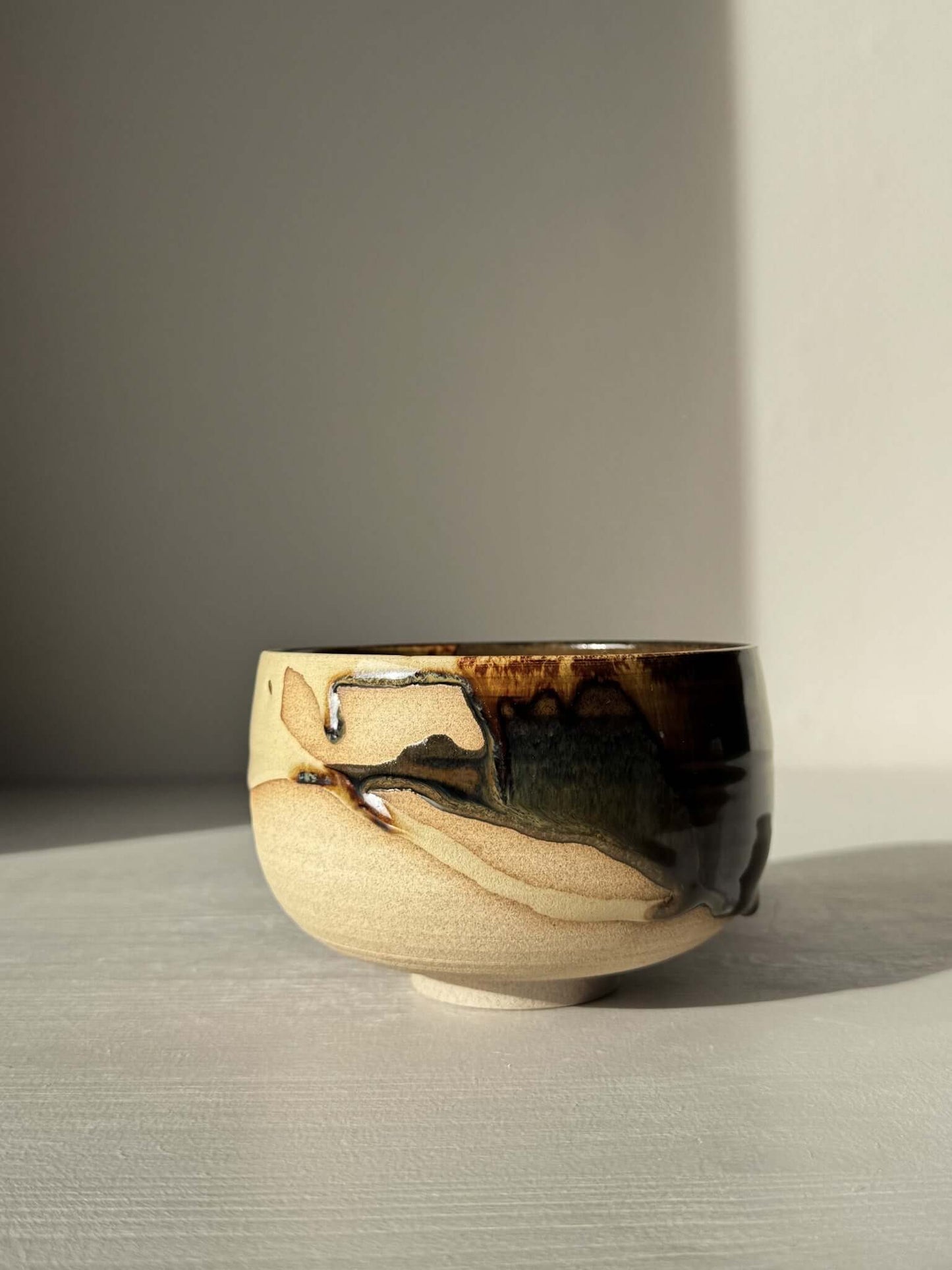 Handmade ceramic Matcha Bowl – Inyo #06 with unique tenmoku and clear glaze on stoneware, displayed in natural light.