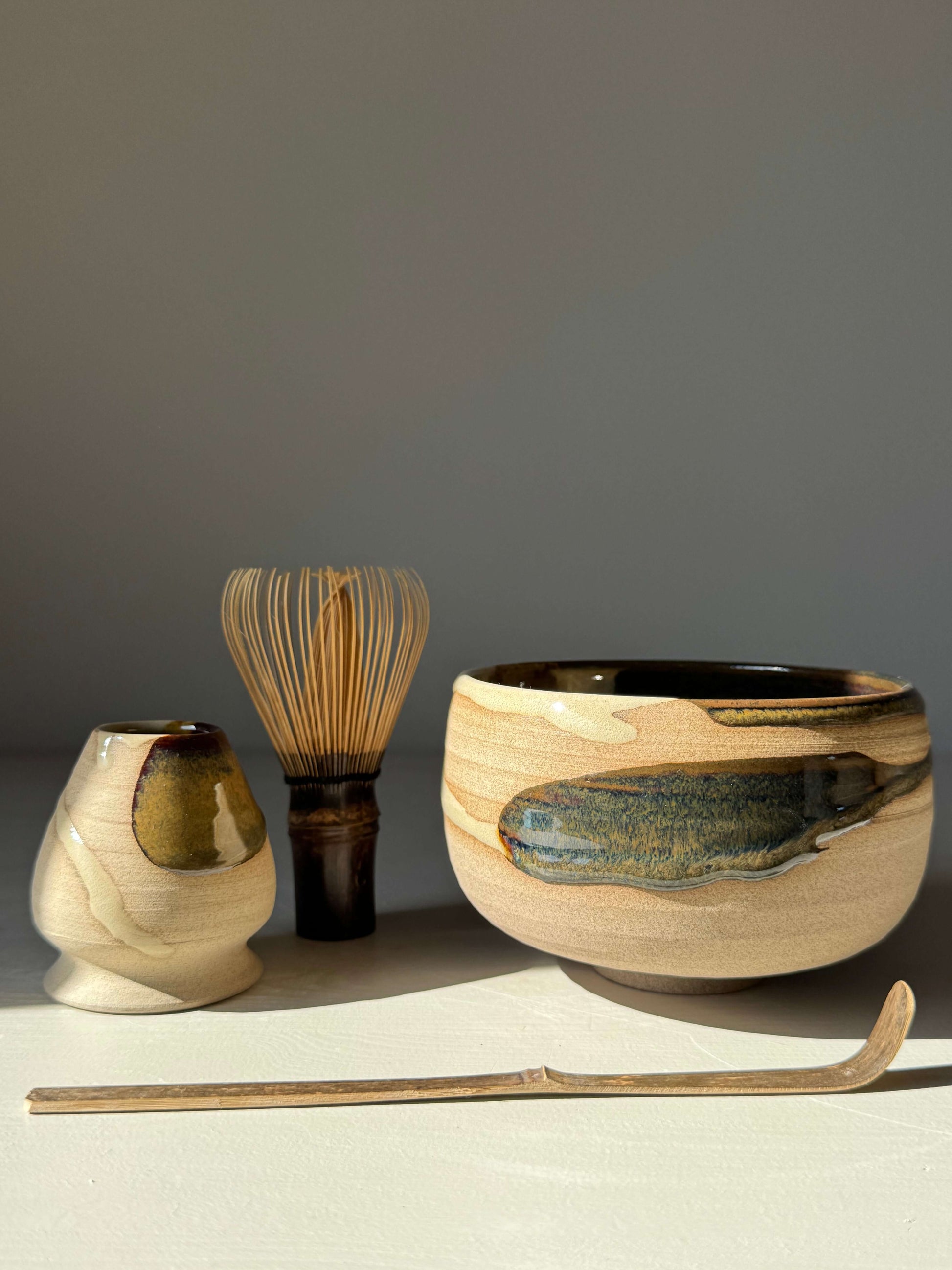 Matcha Bowl – Inyo Series #01, handmade ceramic with glossy tenmoku and clear glaze, shown with whisk and scoop on light background.