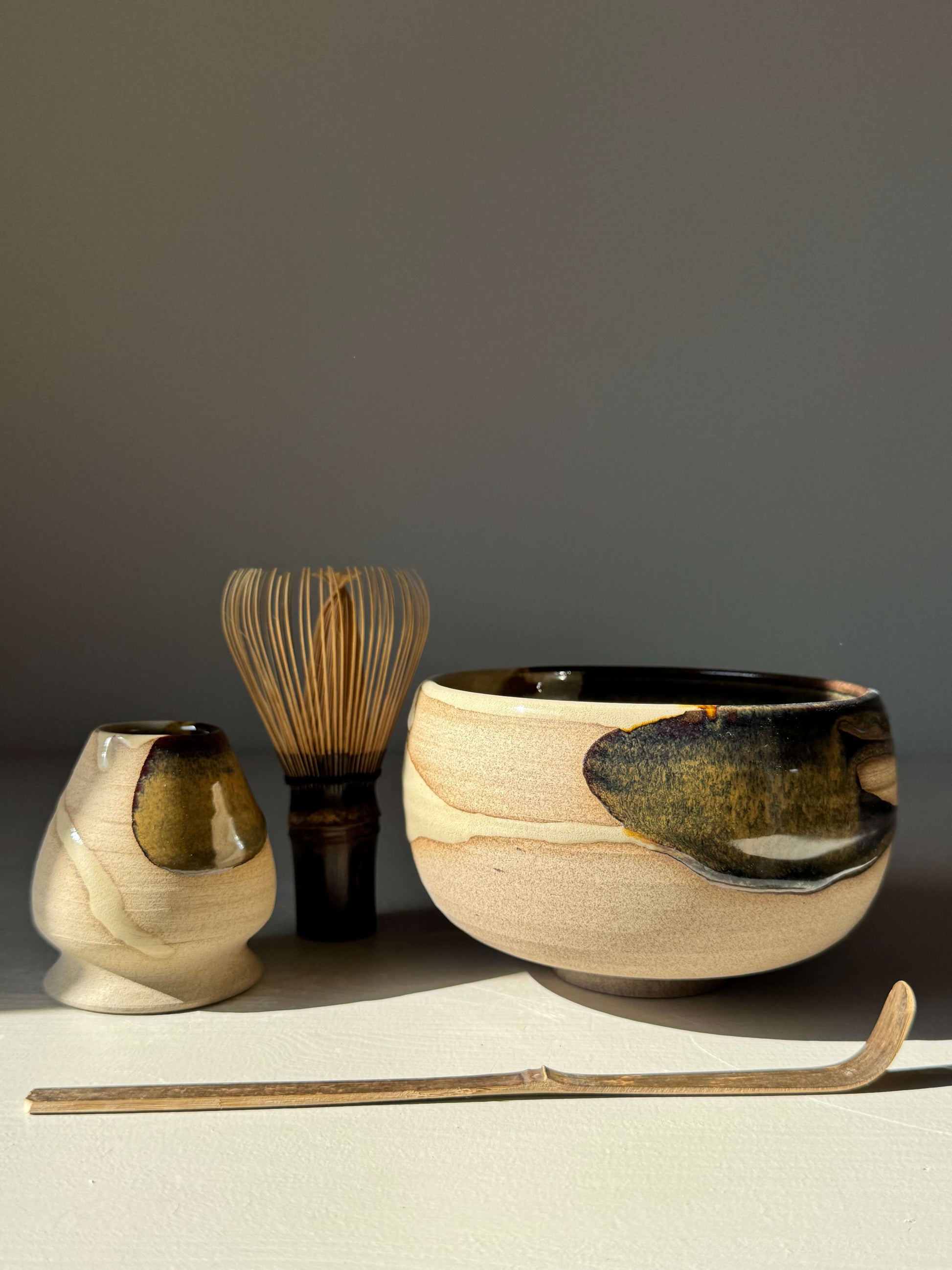 Matcha Bowl – Inyo Series #06, a handmade ceramic with tenmoku and clear glaze, alongside matcha accessories, on a light surface.