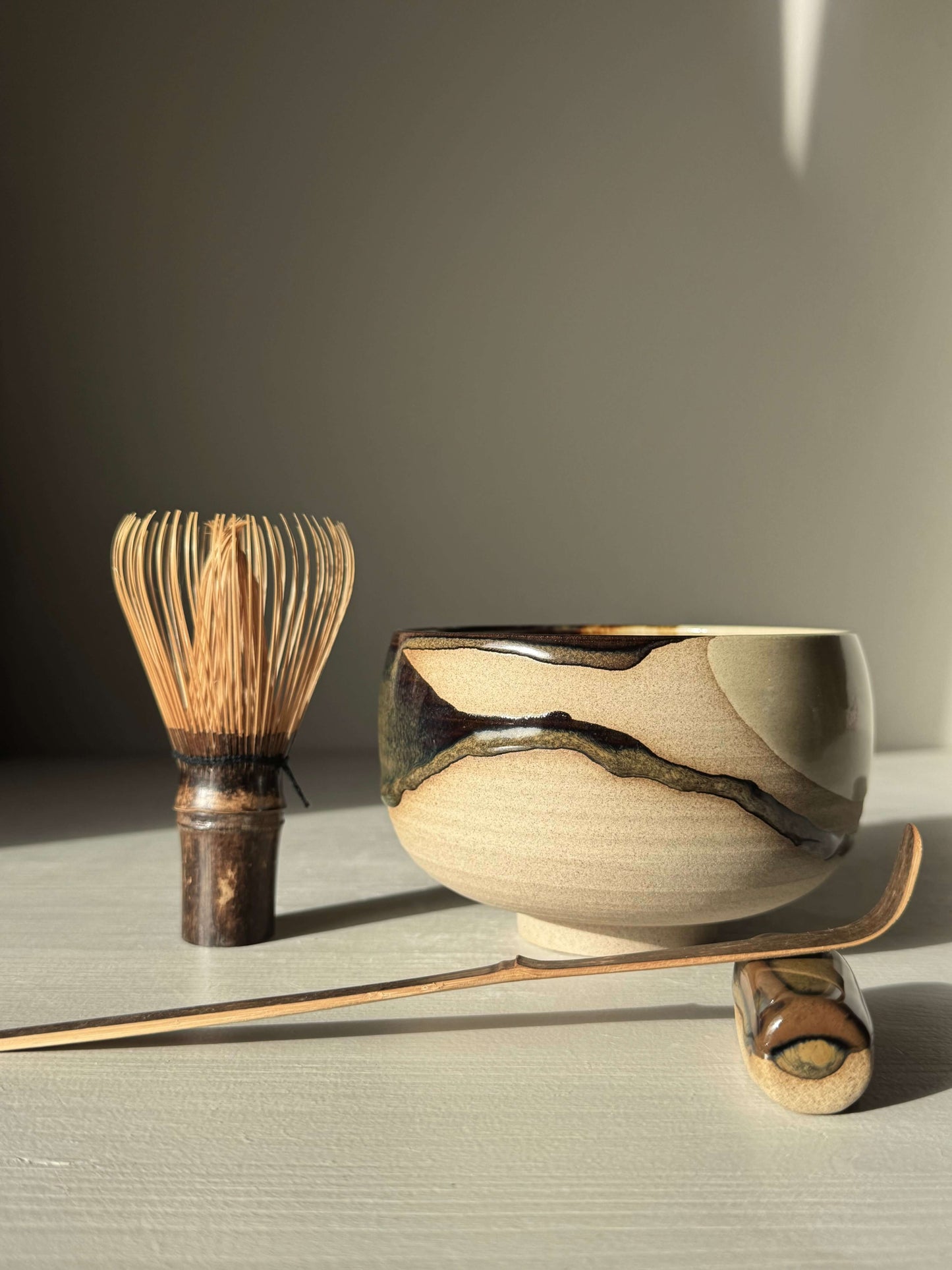 Handmade ceramic Matcha Bowl – Inyo #05 with tenmoku and clear glazes on stoneware, pictured with bamboo whisk and scoop.