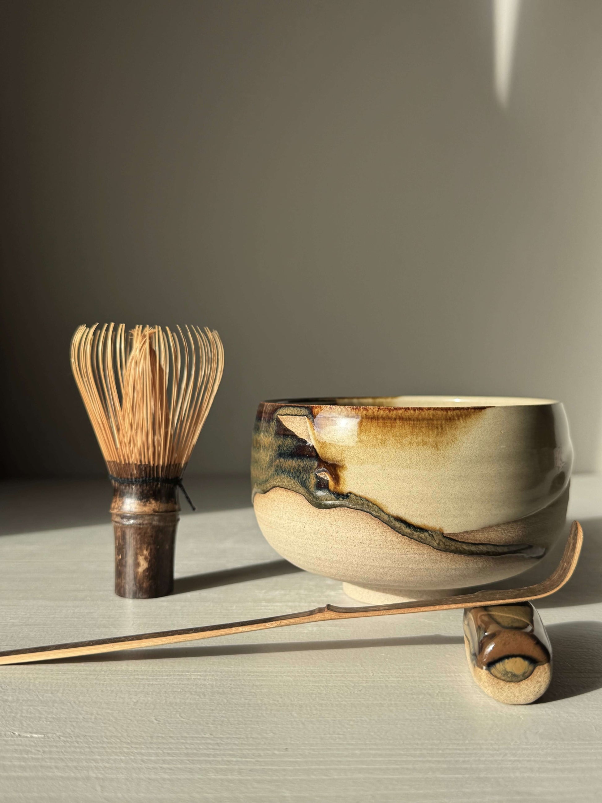 Matcha Bowl – Inyo #03 with handmade ceramic design featuring dark tenmoku and clear glazes, plus tea whisk and scoop on display.