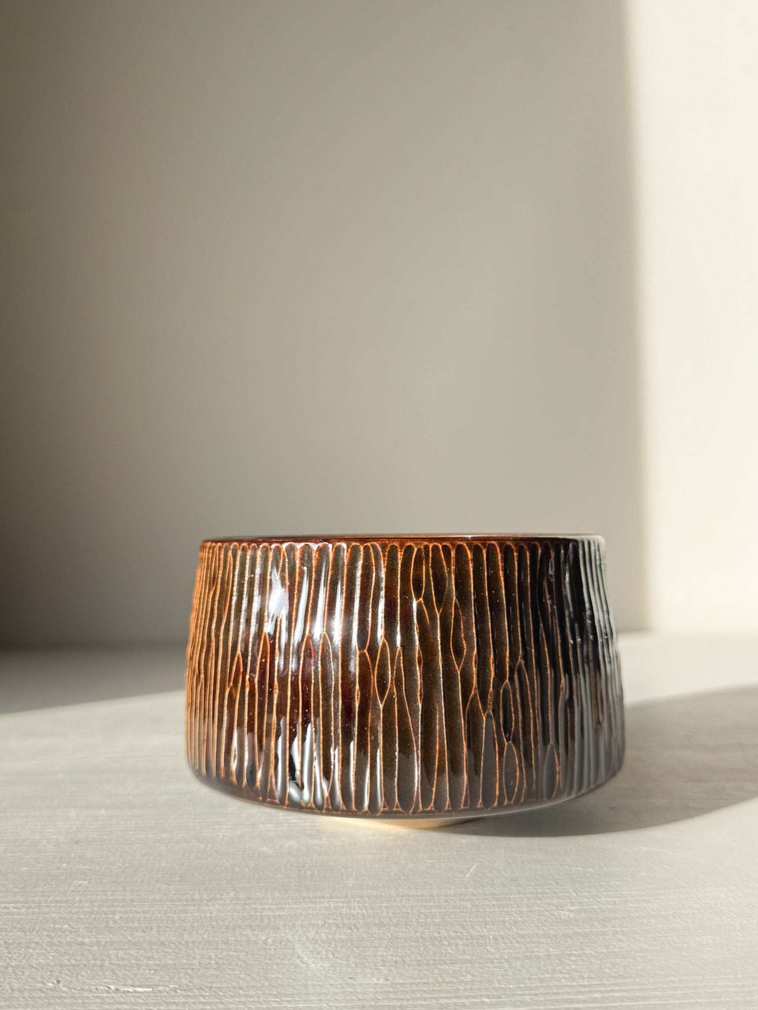 Hand-carved Matcha Bowl – Kinsei #01 with vertical lines and glossy swirl glaze, brown and golden hues, sunlit design.