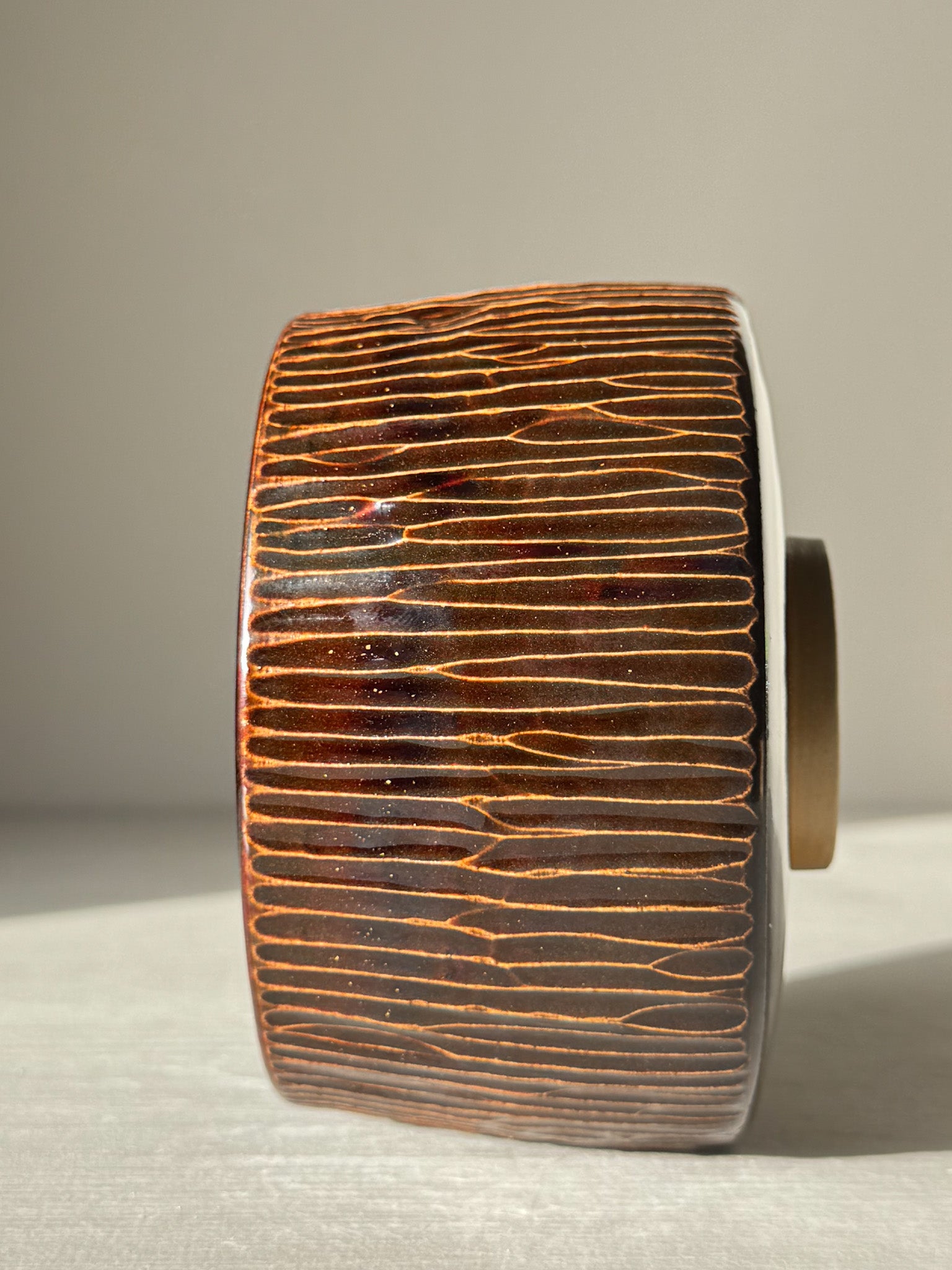 Hand-carved Matcha Bowl – Kinsei #01 with deep brown and golden glaze highlighting intricate vertical design under light.