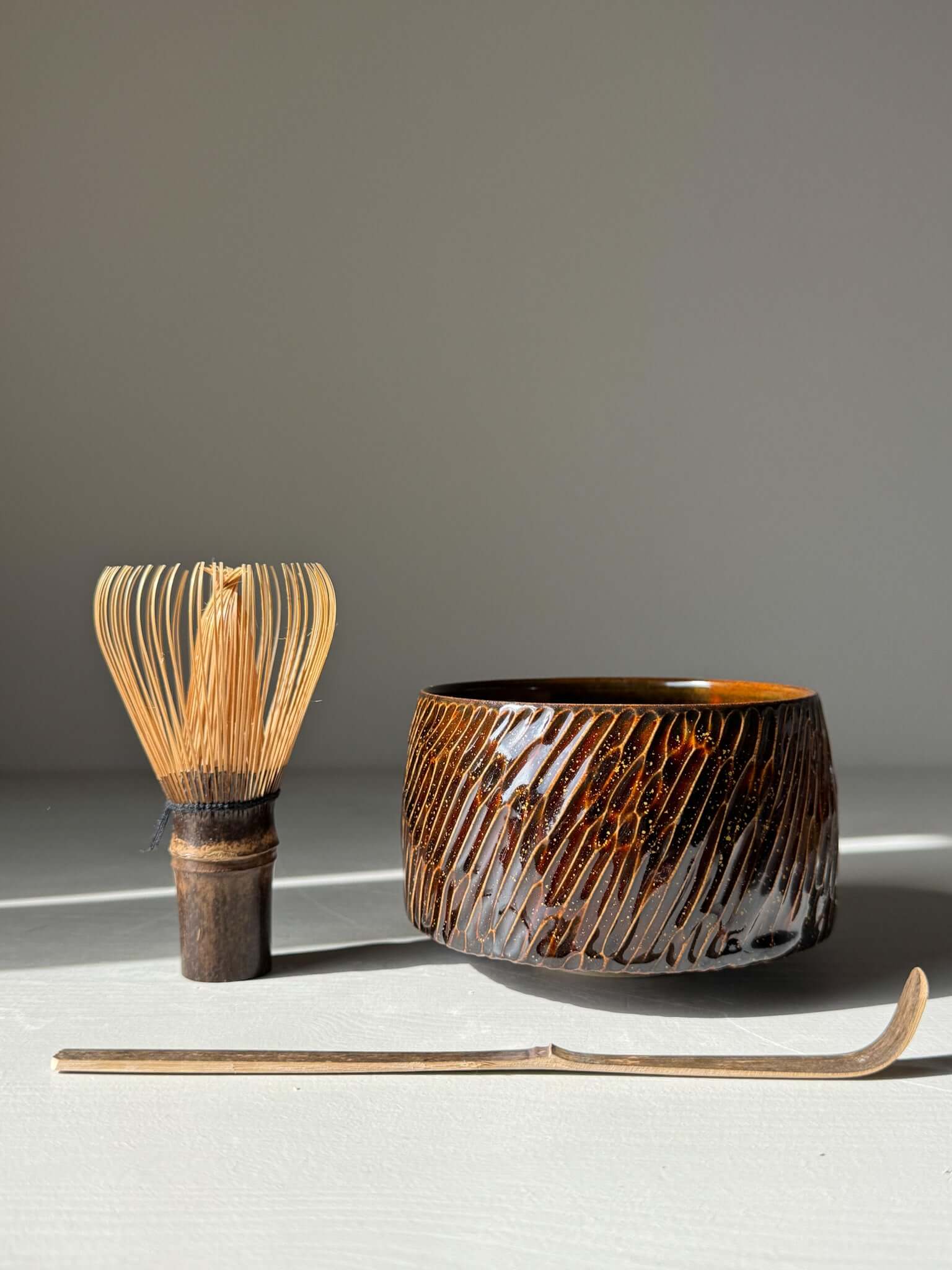 Handmade ceramic Matcha Bowl – Kinsei #05 with carved glossy brown exterior, spiral gold interior, and matcha whisk on display.