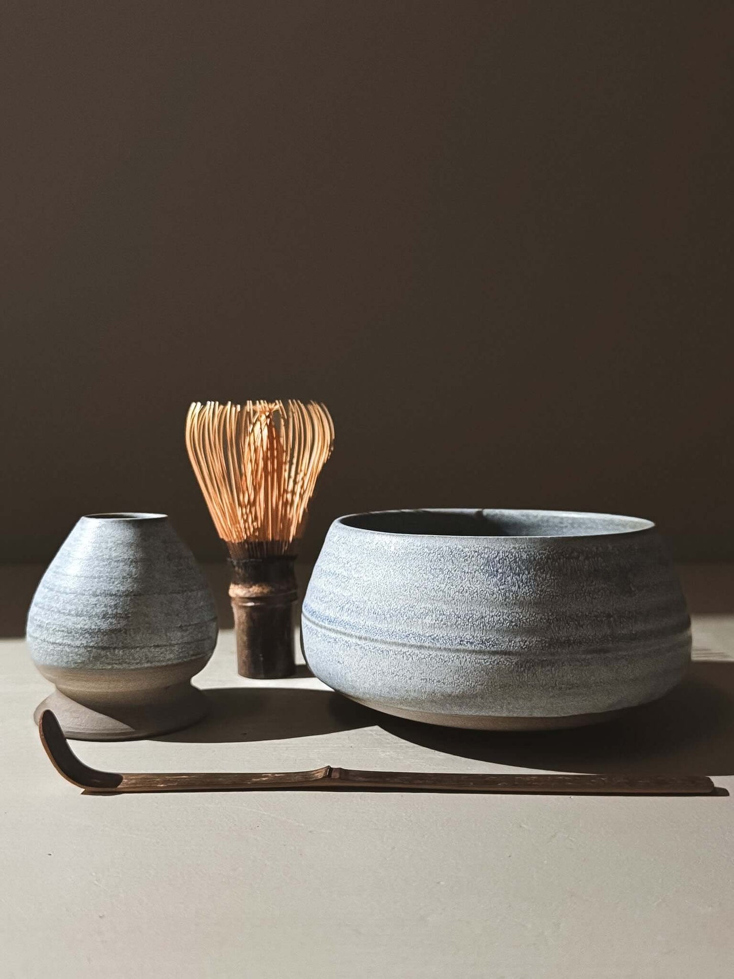 Matcha Bowl - Mizu #04 with matte blue glaze and dark clay foot, surrounded by traditional matcha utensils for tea preparation.