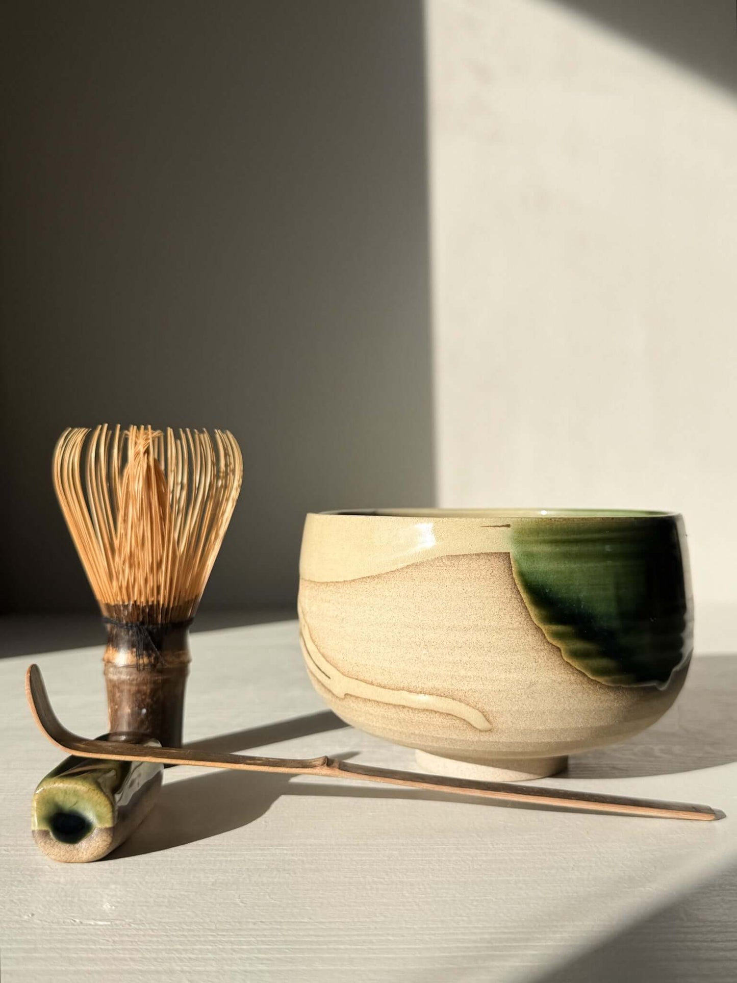 Handmade ceramic Matcha Bowl – Mori #01 with natural stoneware and green-brown glazes, accompanied by a bamboo tea whisk and scoop.