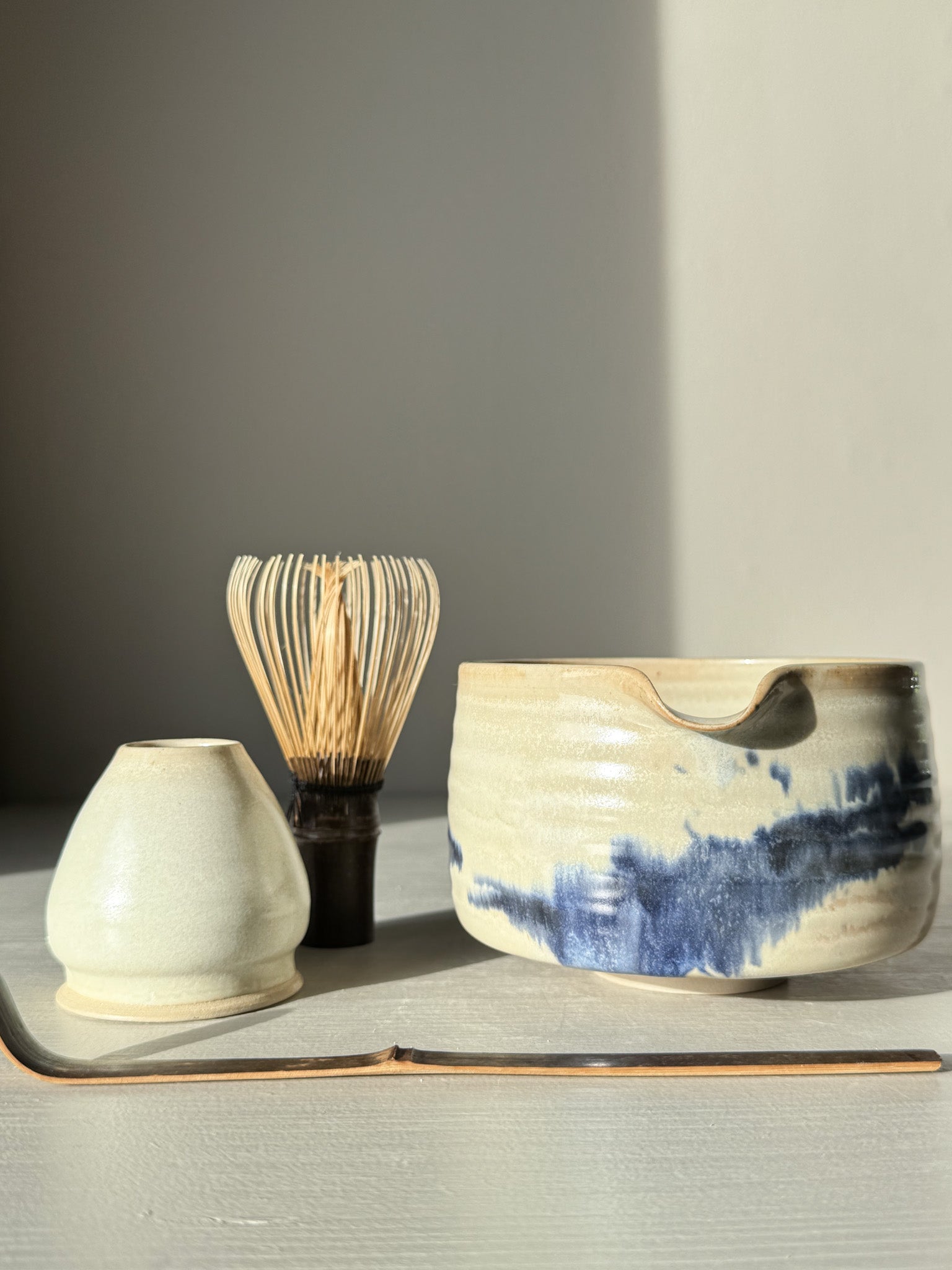 Matcha bowl Spout - Moonstone & Blue #03 with hand-splashed cobalt glaze beside matcha whisk and scoop on a tabletop.
