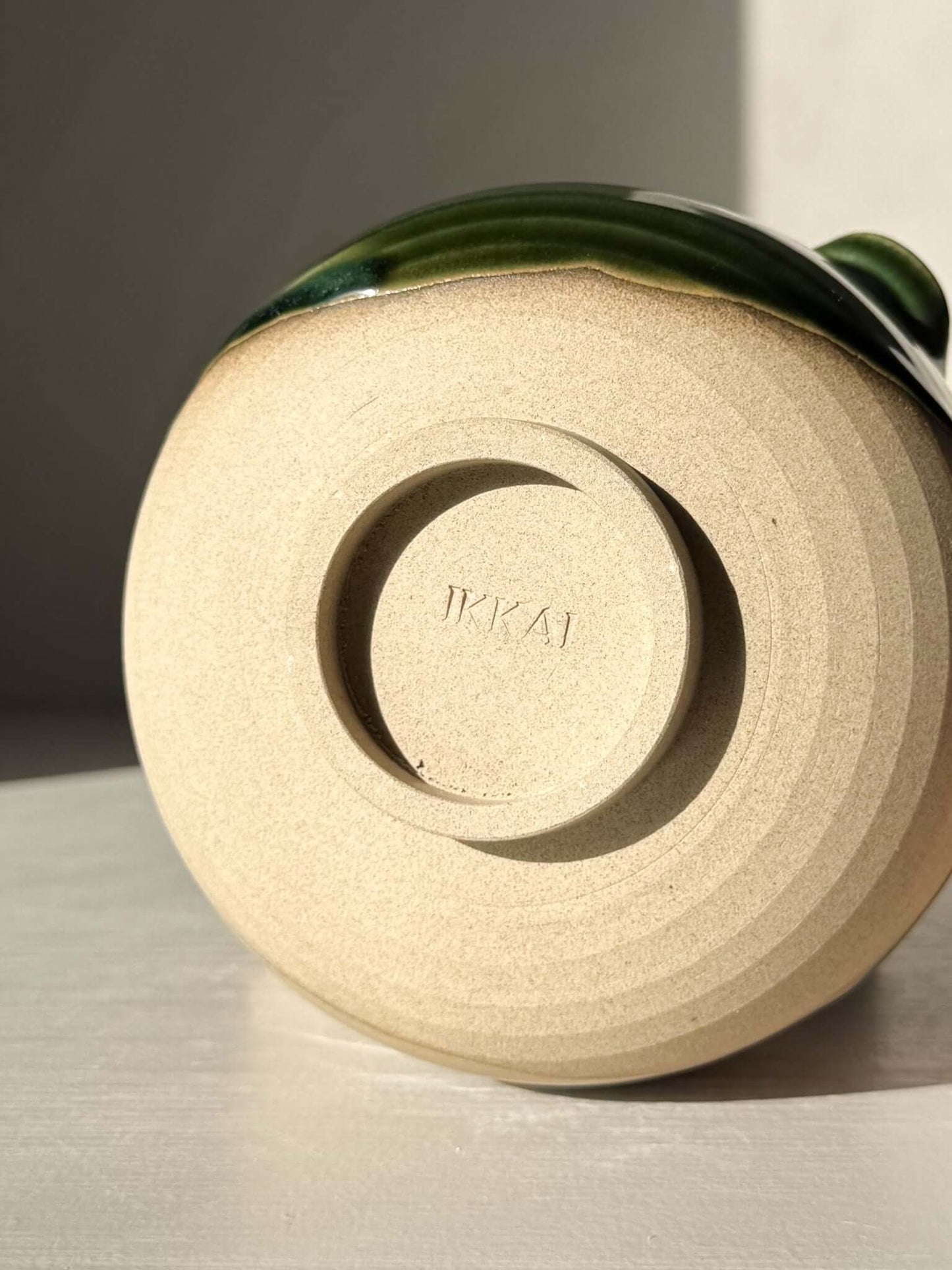 Base of handmade ceramic Matcha Bowl with Spout – Mori #01 showing natural stoneware texture, green glaze, studio marking 'TKAI'