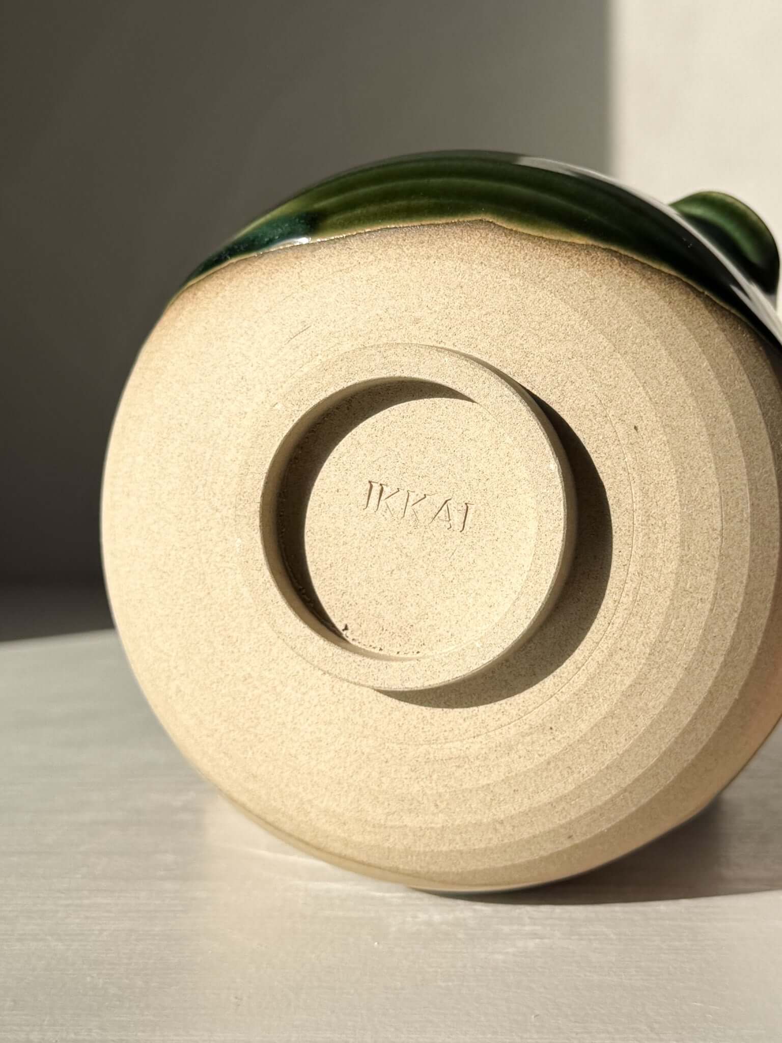 Base of handmade ceramic Matcha Bowl with Spout – Mori #01 showing natural stoneware texture, green glaze, studio marking 'TKAI'