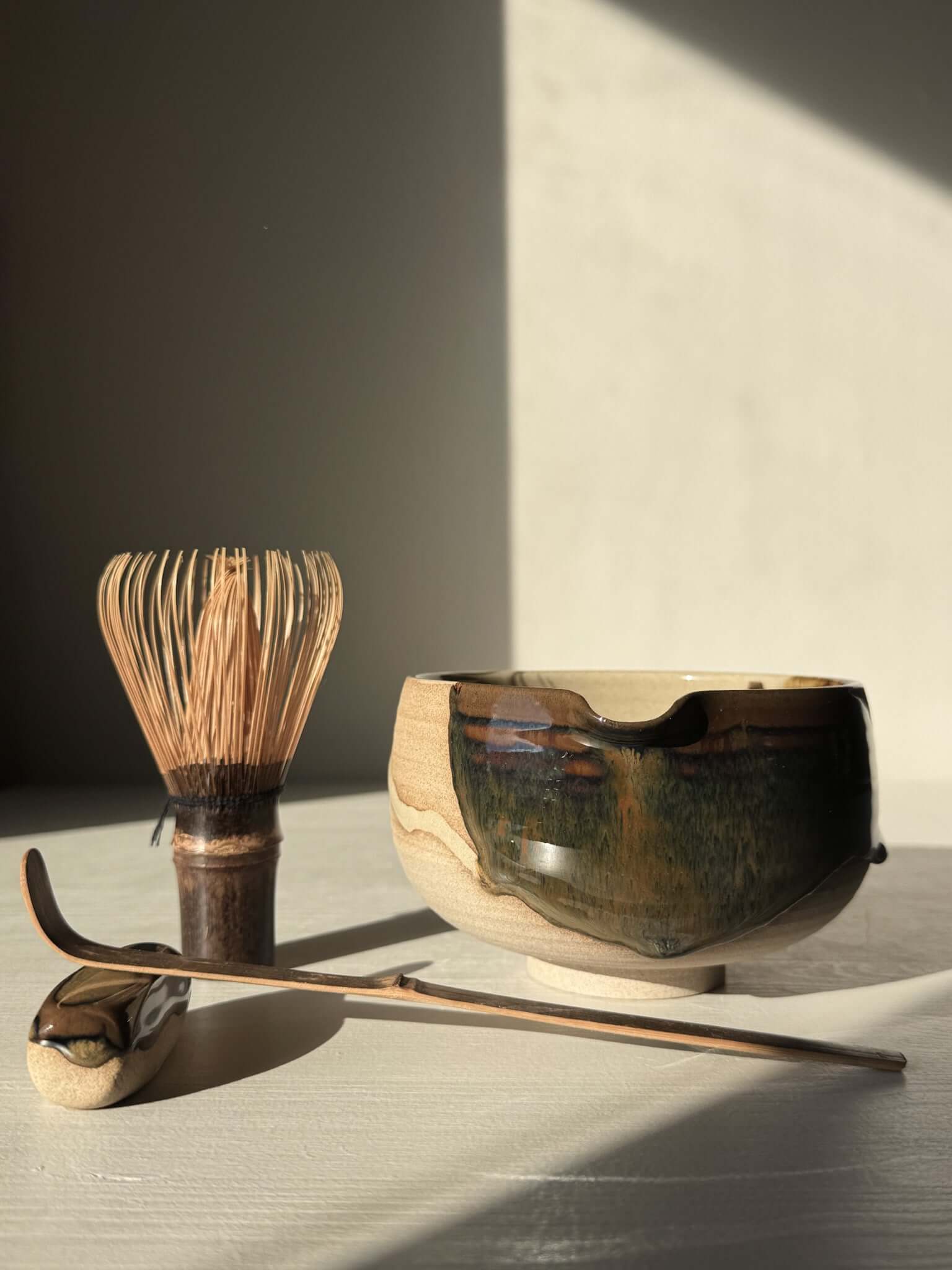 Handmade Matcha Bowl with Spout – Inyo #02 with whisk and scoop on a table, featuring glossy tenmoku and clear glazes.