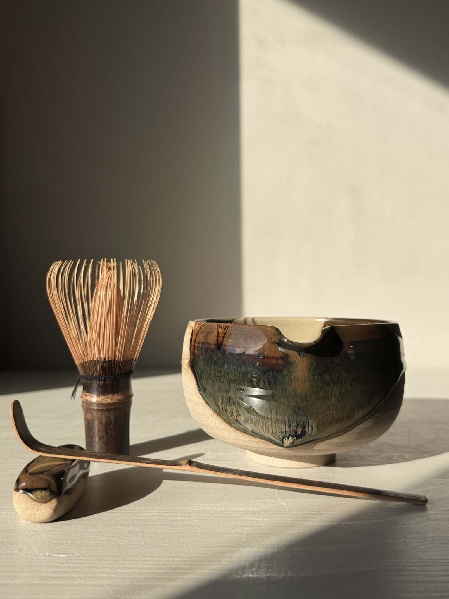 Handmade ceramic Matcha Bowl with Spout – Inyo #04 featuring tenmoku and clear glazes, alongside bamboo whisk and spoon.
