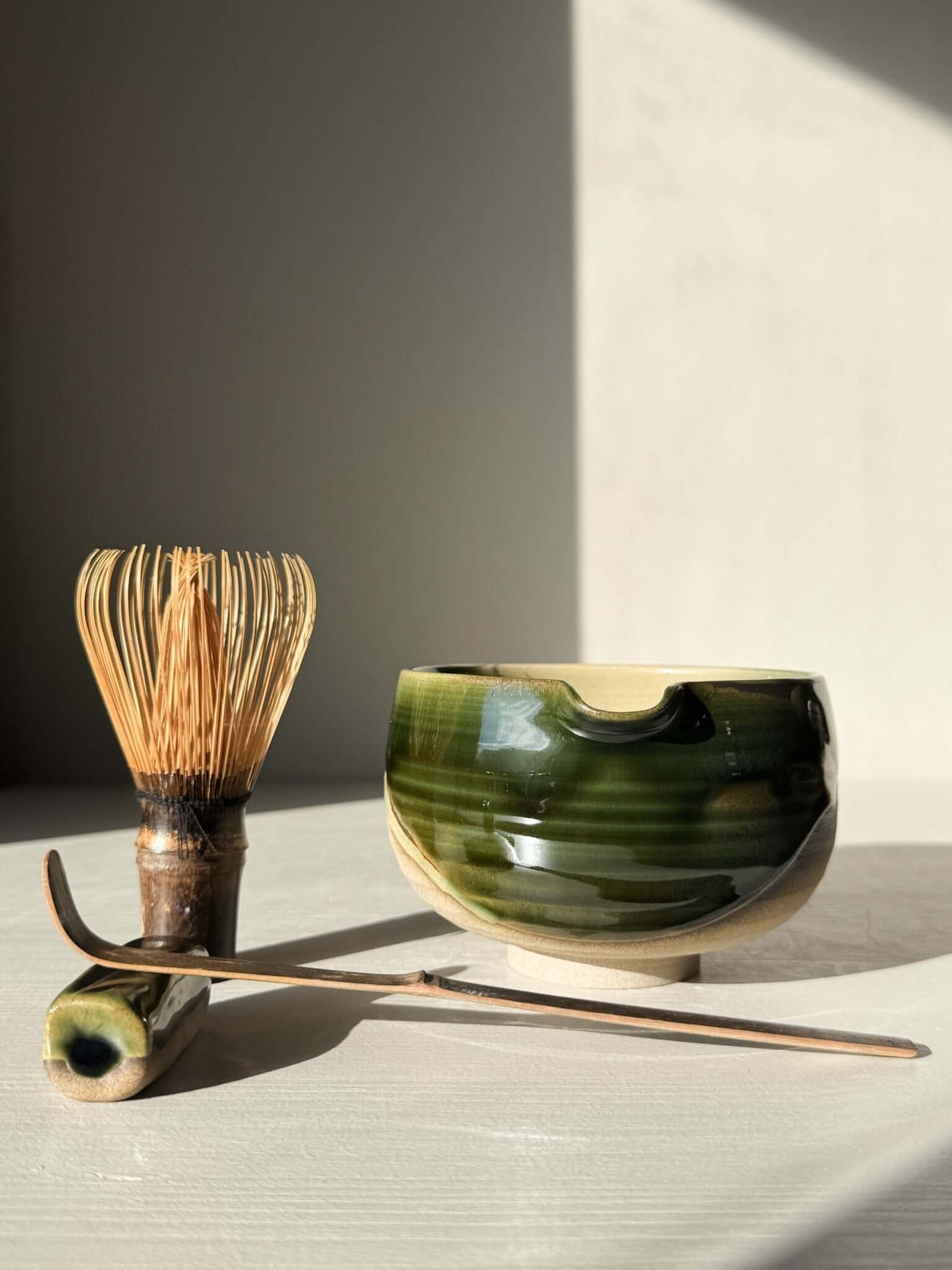 Handmade ceramic Matcha Bowl with Spout – Mori #04 with green and brown glaze, alongside matcha whisk and spoon.