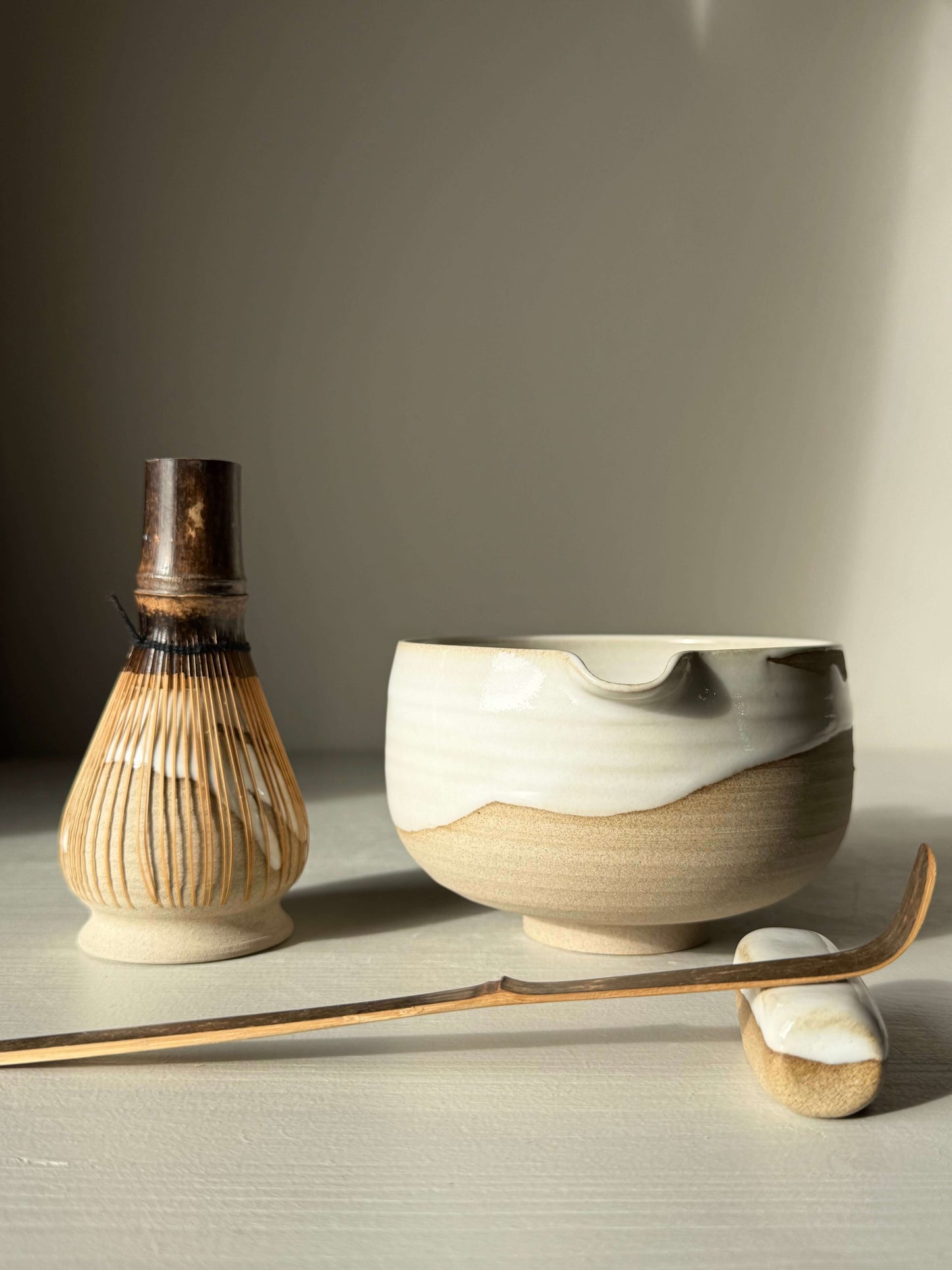 Handmade ceramic Matcha Bowl with Spout – Yuki #01 featuring toffee clay and white glaze, accompanied by bamboo whisk and spoon.